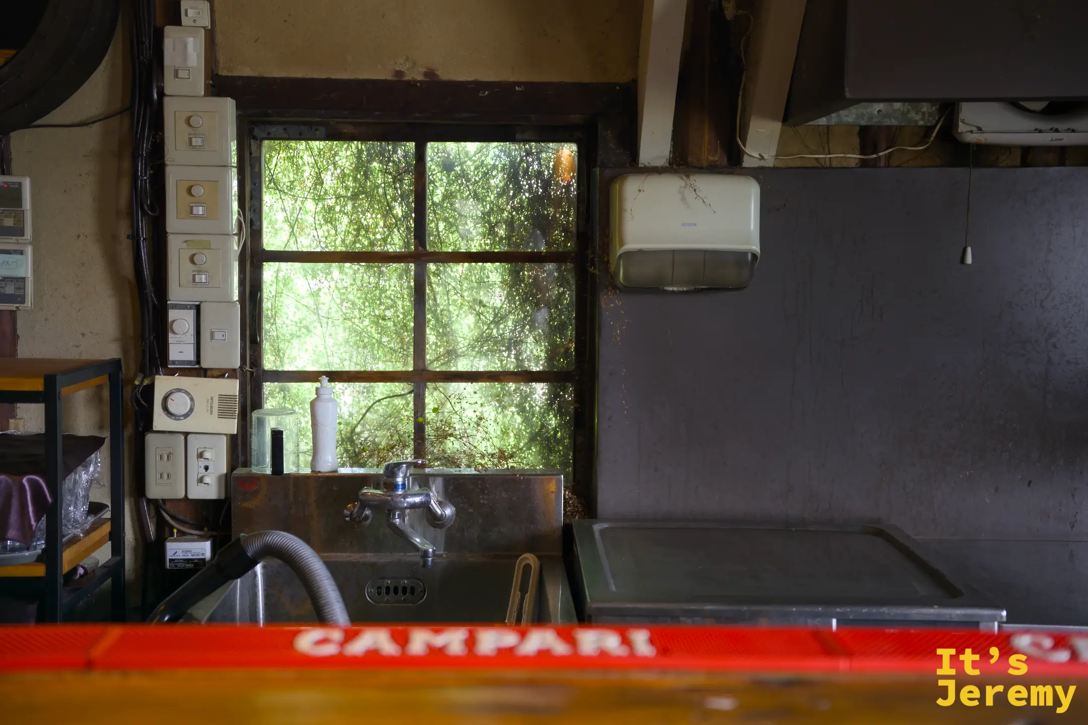 倉庫改建的室內空間，格子木窗透進光線，前景是一台紅色 CAMPARI 冰櫃與座位