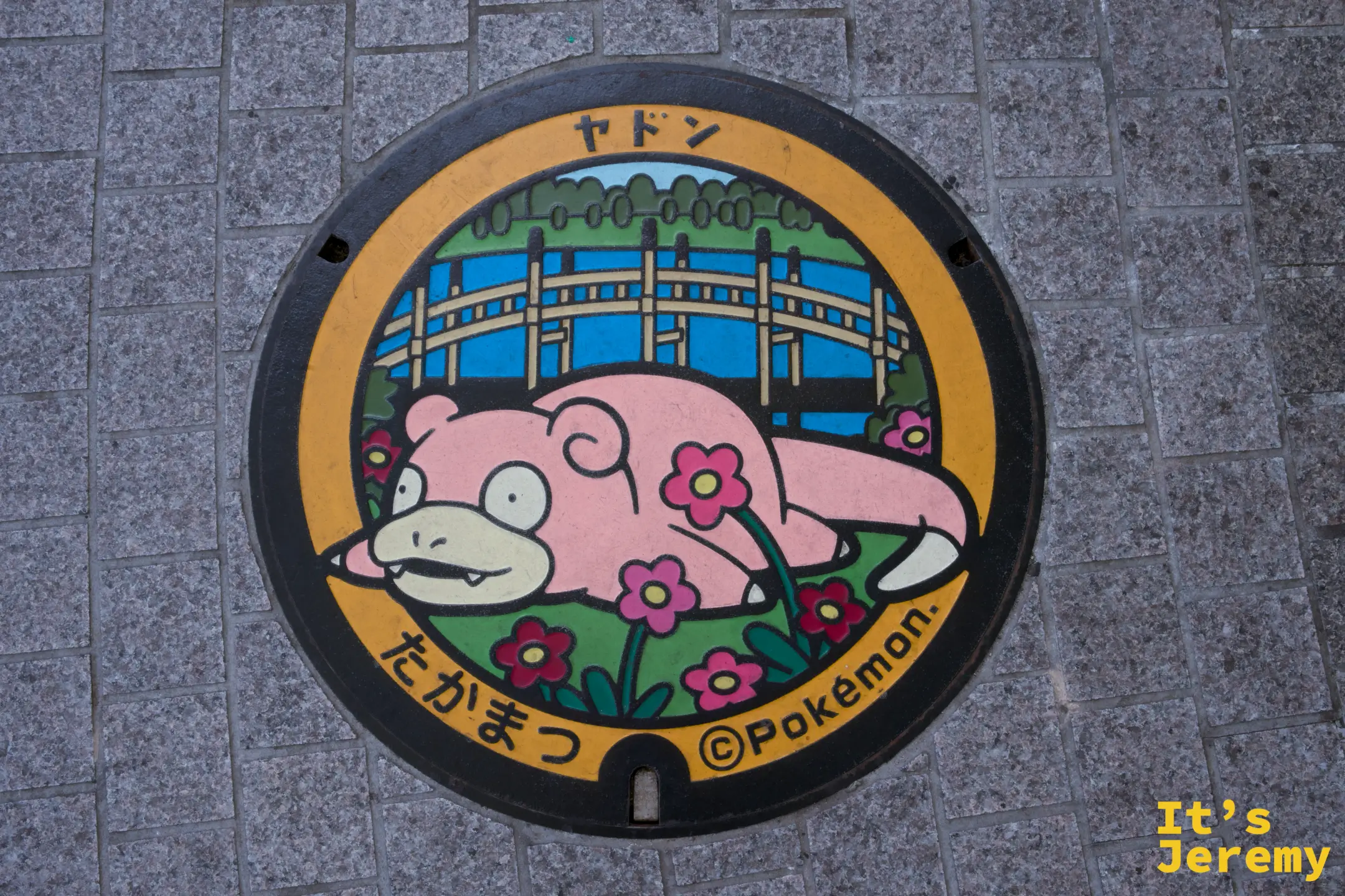 圓形人孔蓋，橙色邊框，中央繪有呆呆獸趴臥於花草間，印「ヤドン」與「たかまつ」字樣