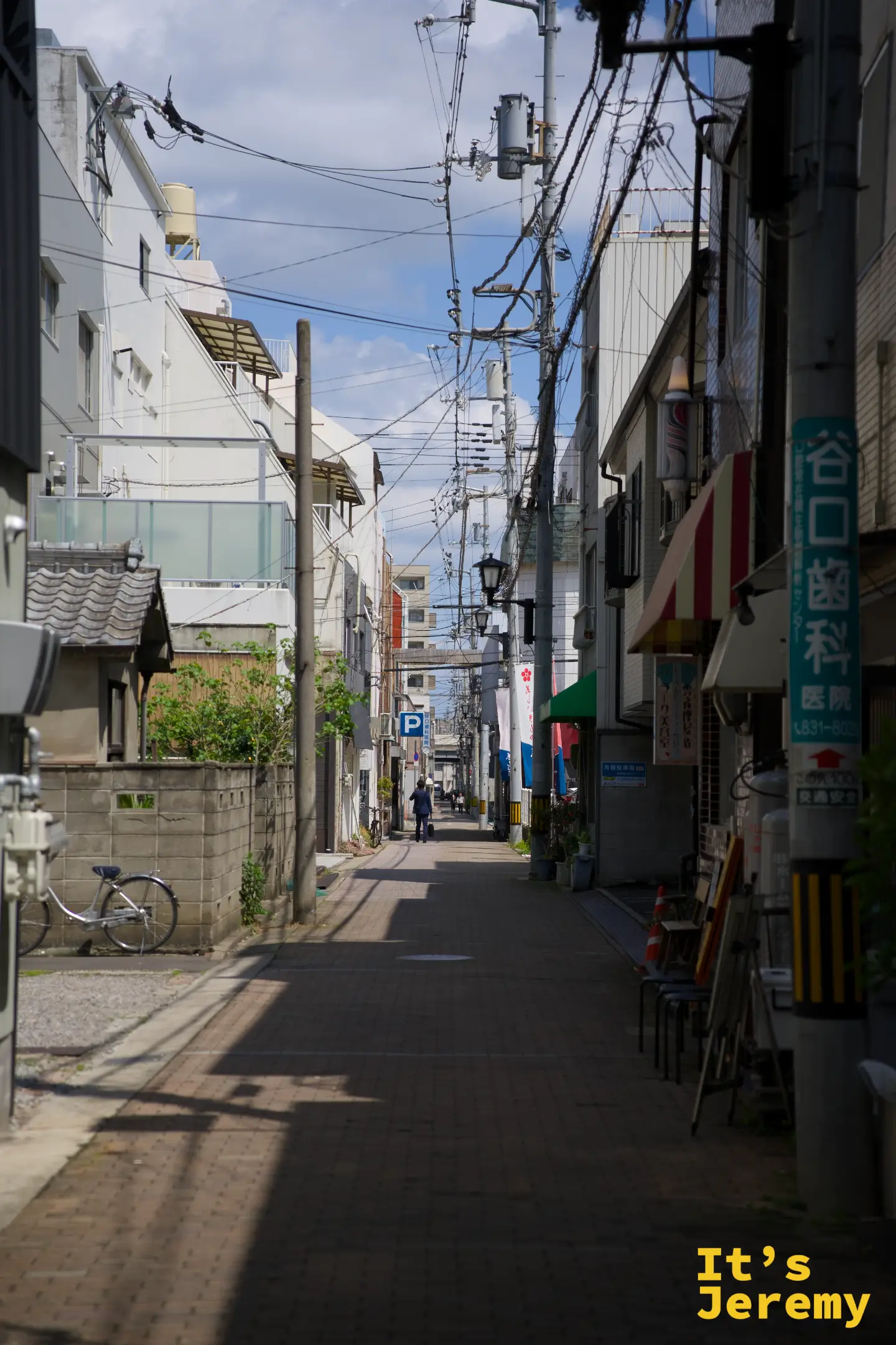 丸亀町周邊的住宅巷弄，電線桿與低矮建築夾出一條安靜的小路，遠處有一名路人往前走