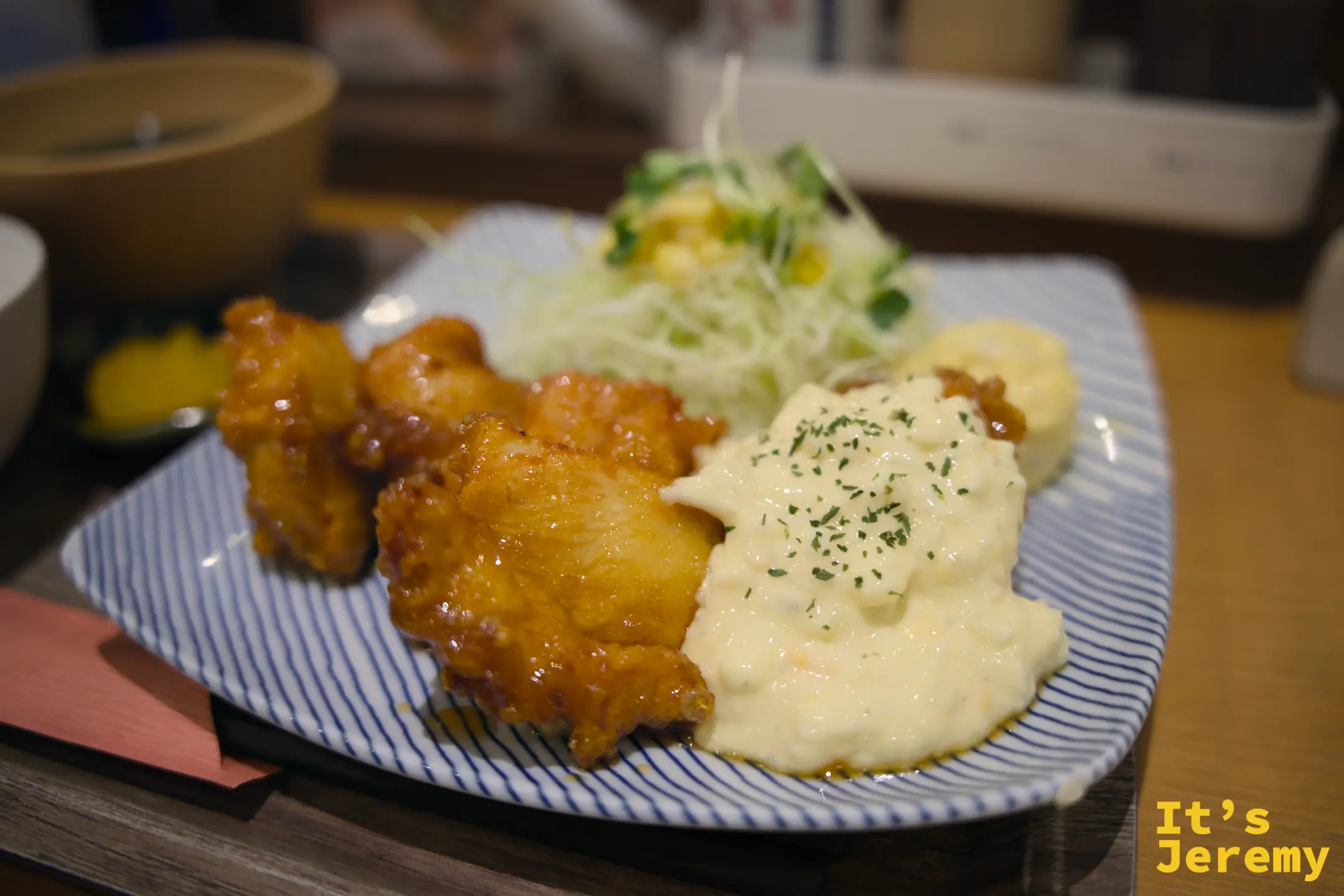 チキン南蛮特寫，金黃色的炸雞塊搭配白色奶香美乃滋醬，旁邊是高麗菜絲和玉米沙拉，擺在藍白條紋盤上