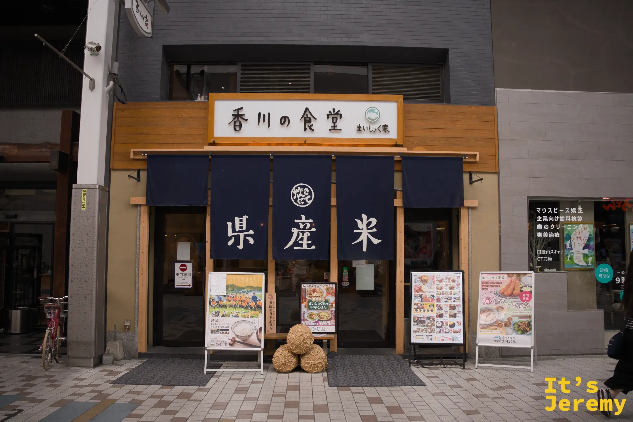 香川の食堂 まいしょく家 外觀，深藍色暖簾上書「縣産米」三字，入口前擺著稻草造型展示物