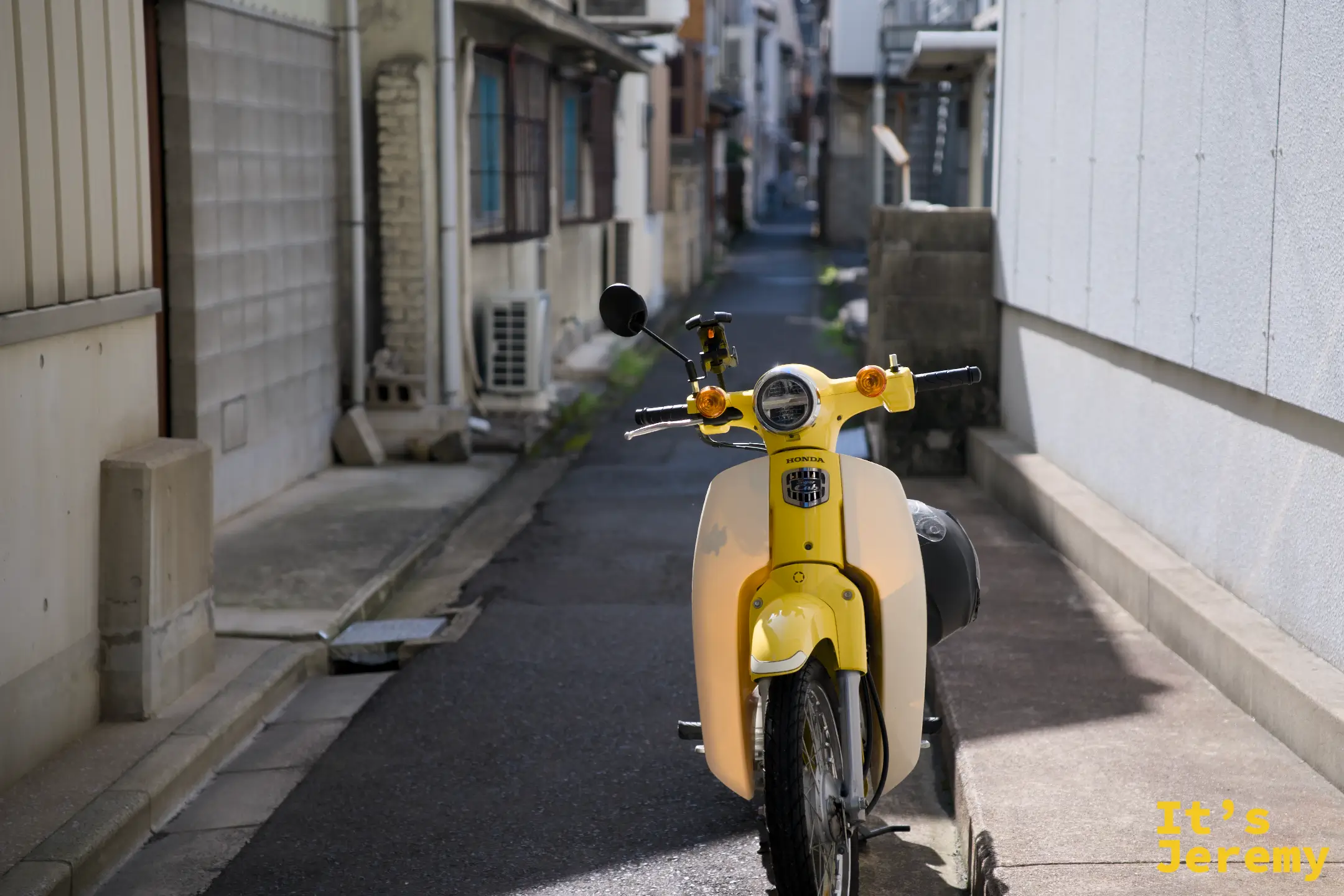 丸亀町一帶住宅小巷，一輛亮黃色 Honda 老摩托車停在灰色牆面前，光線從巷口一端斜斜打進來