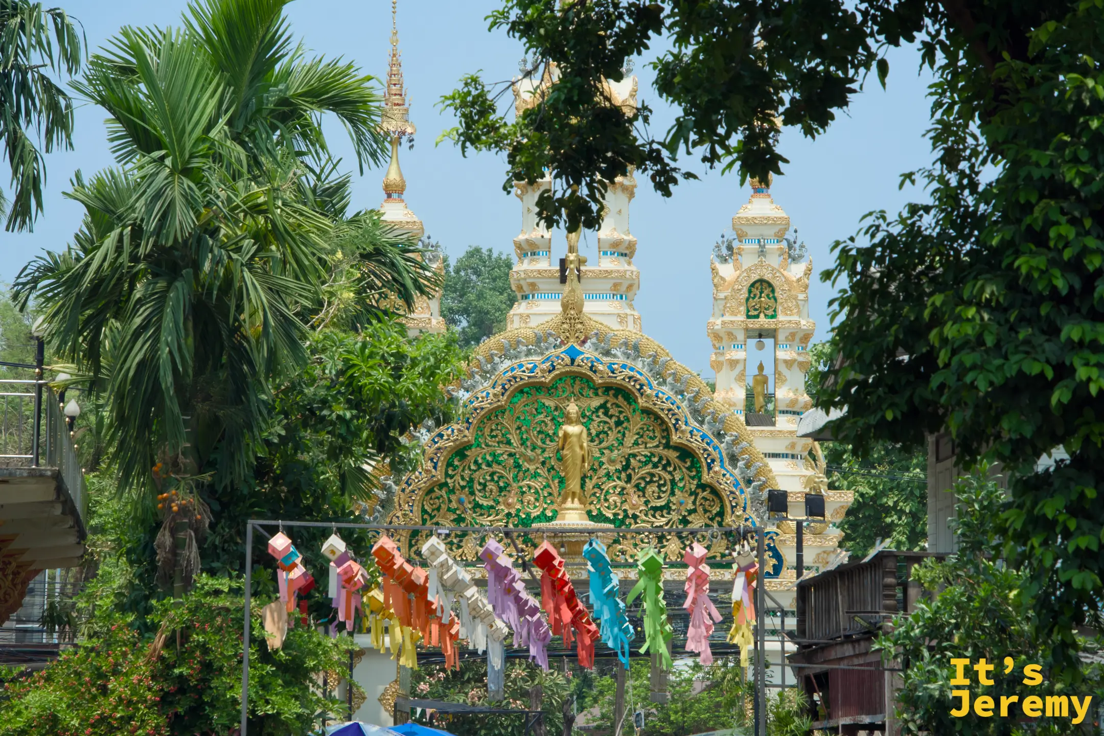 Wat Lam Chang 主牌樓正面，綠金色拱頂嵌有金色立佛，牌樓前多色布旗層層垂掛，色彩繽紛