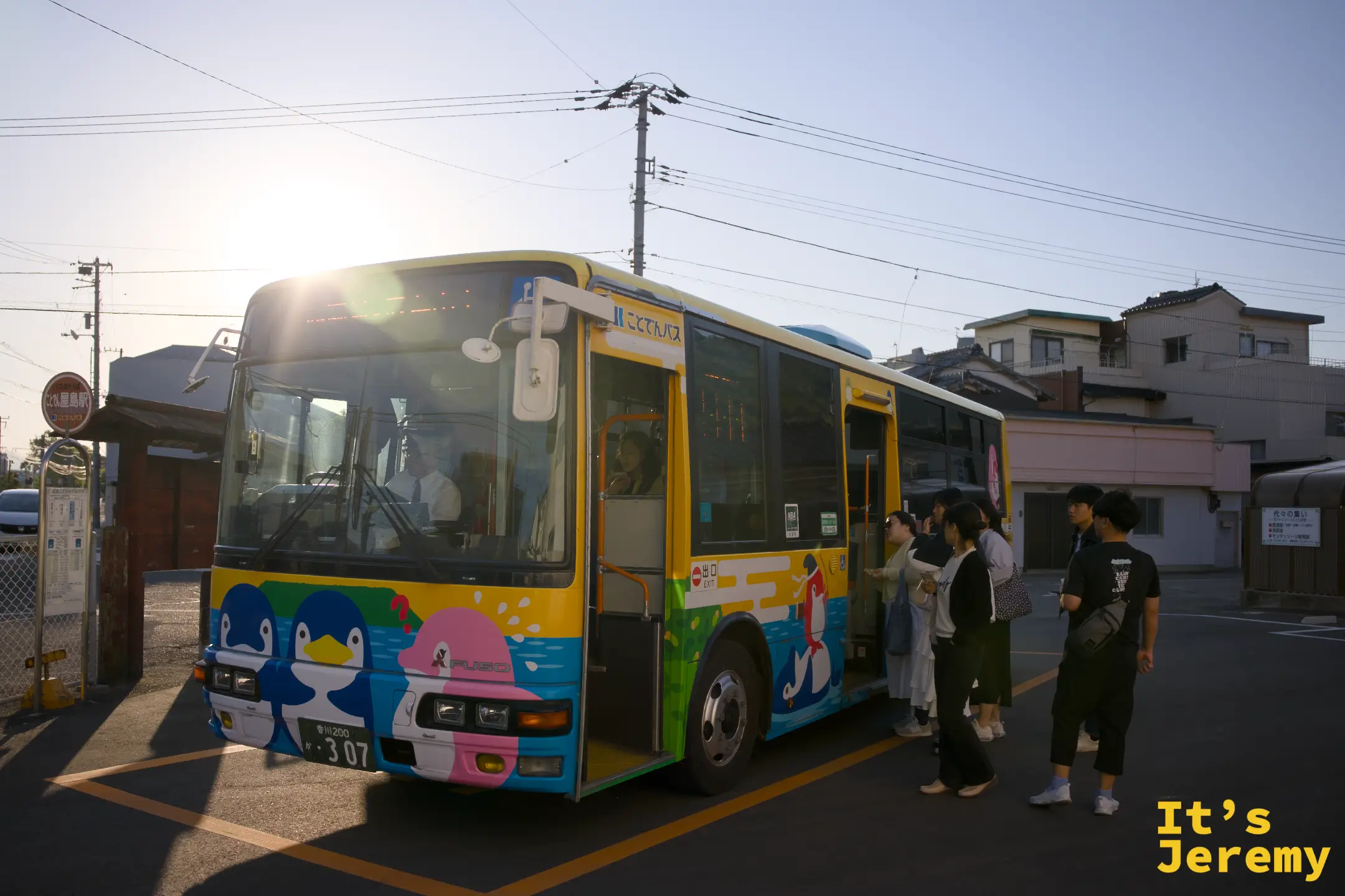 繪有海豚圖案的屋島山上シャトルバス，幾位旅客正在排隊上車，夕陽從車後灑進來