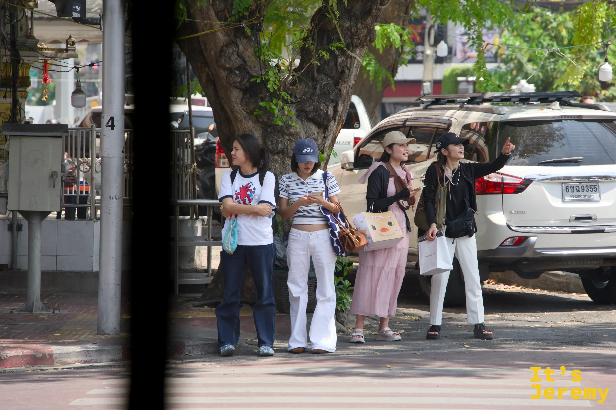 對街四個穿復古丹寧的曼谷女生在樹蔭下伸手攔車，週間下午的老城區一景