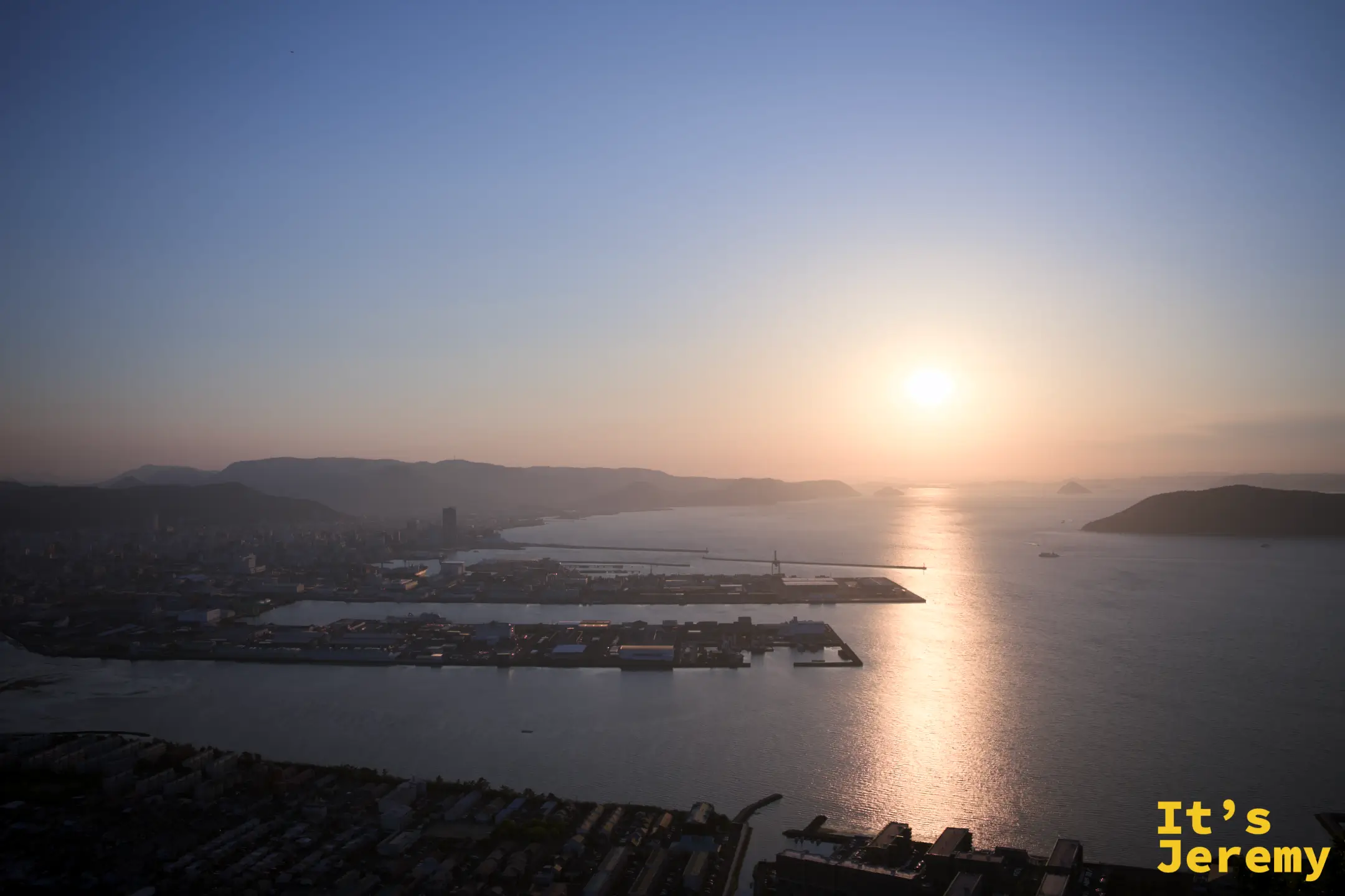傍晚，從屋島展望台俯瞰高松港和瀨戶內海，太陽偏低，港口碼頭和防波堤在橙光中清晰剪出