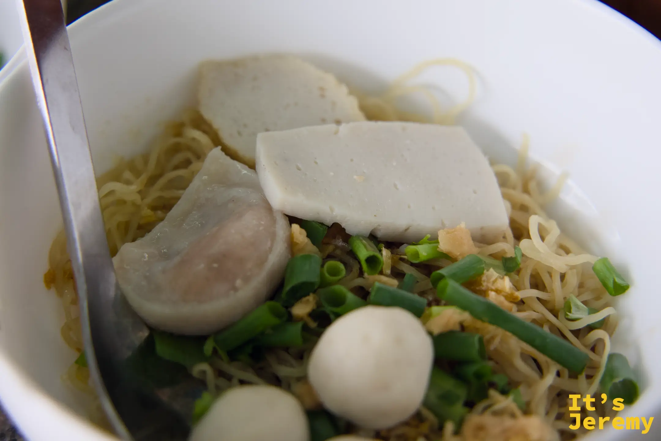 乾拌蛋麵碗,麵條上方鋪著魚丸、魚餅、嫩豆腐與青蔥