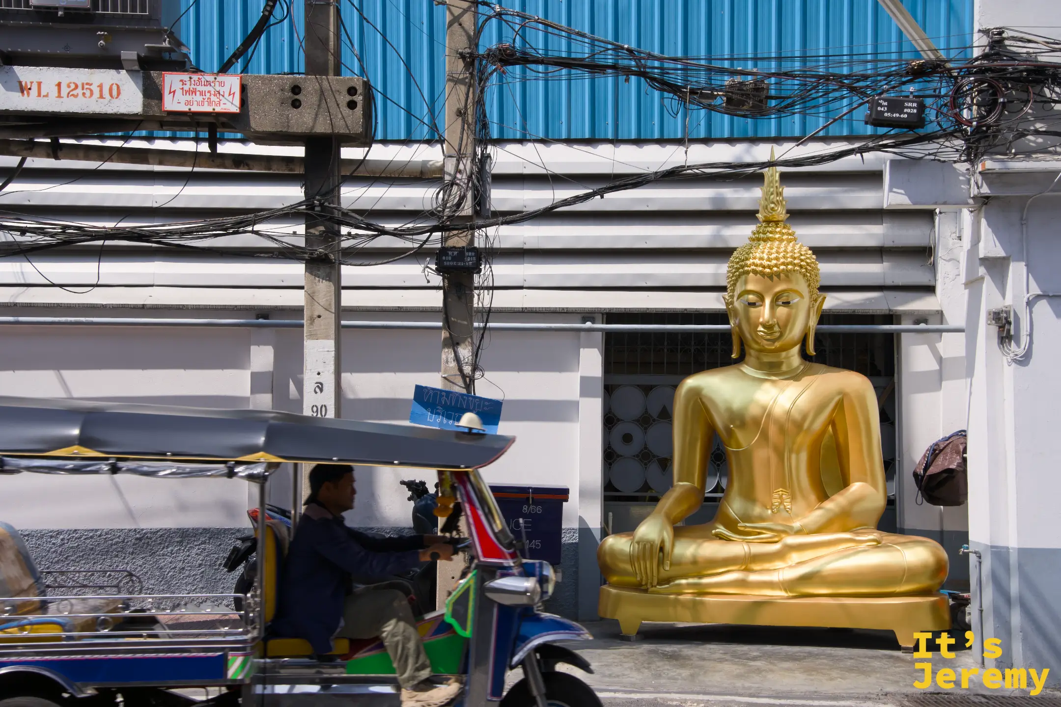 馬路邊一尊真人尺寸的金色坐佛被推到藍色 tuk-tuk 旁，準備被載走