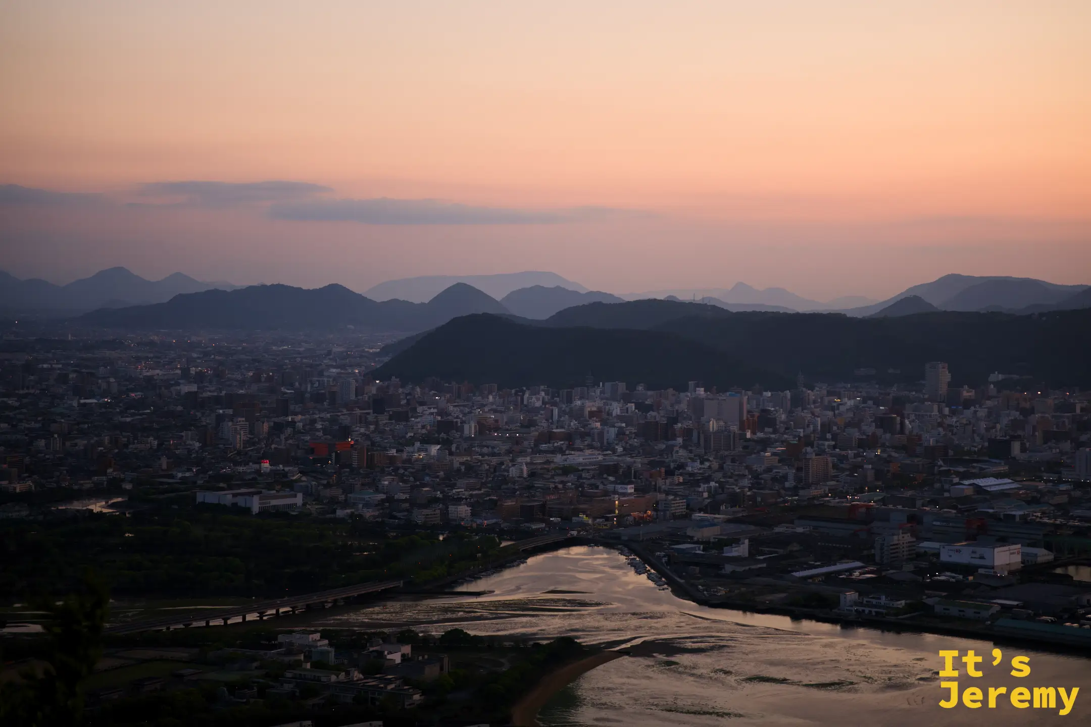 入夜前藍調時刻，高松市區與蓬萊川弧形河道，山脈疊層，城市邊緣燈光稀疏