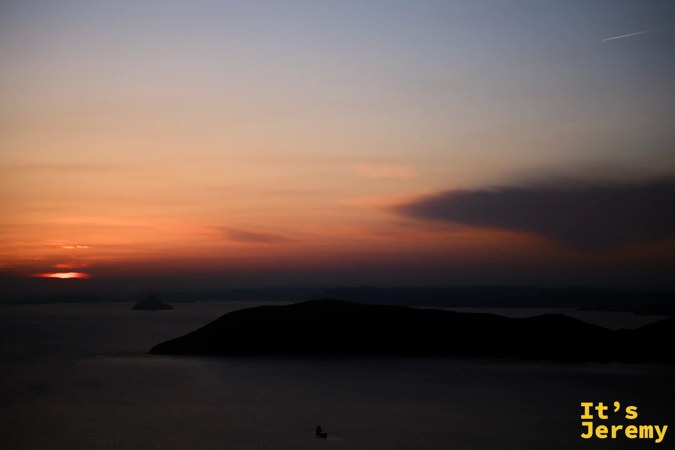 太陽完全沉落，橙紅色餘暉在島嶼邊緣徘徊，海面已失去光澤，一艘小船靜靜穿過畫面