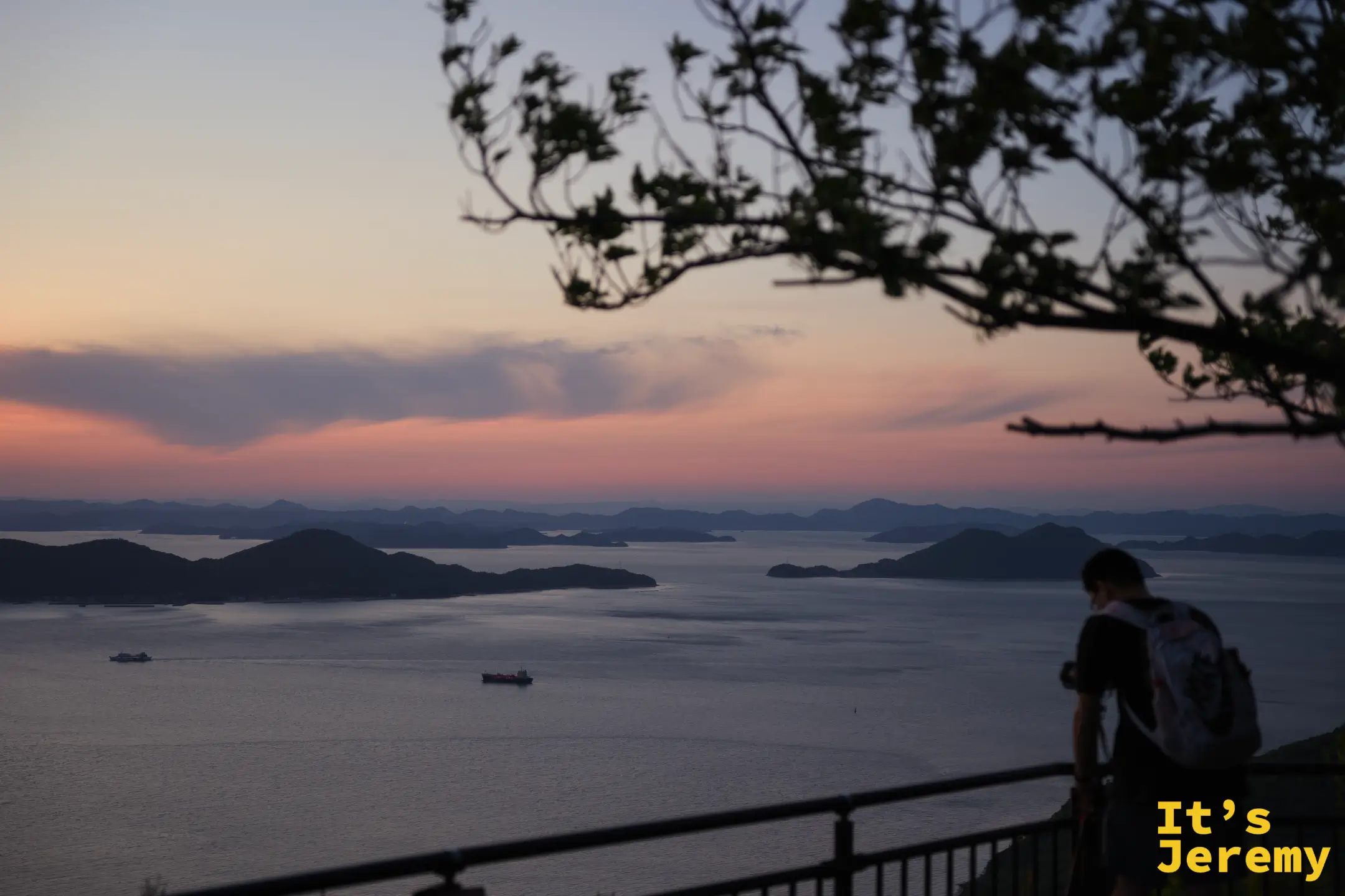 一名背包旅人倚著欄杆俯瞰，瀨戶內海多島景觀在入夜前呈現粉藍色，空氣裡有剛好的靜