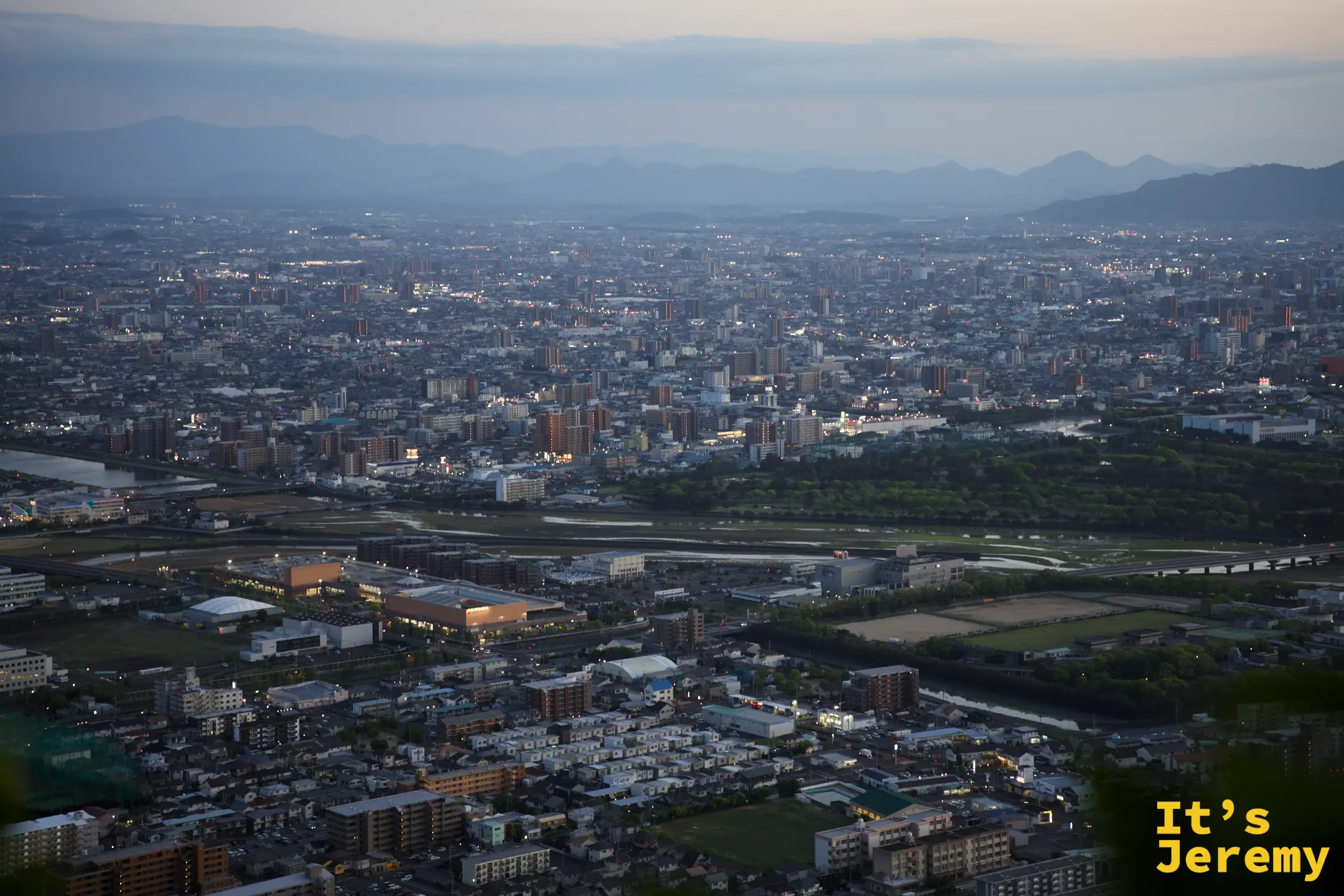 夜色漸深的高松全景，建築群由燈光勾勒出輪廓，河川反光，遠山已完全融入暗色