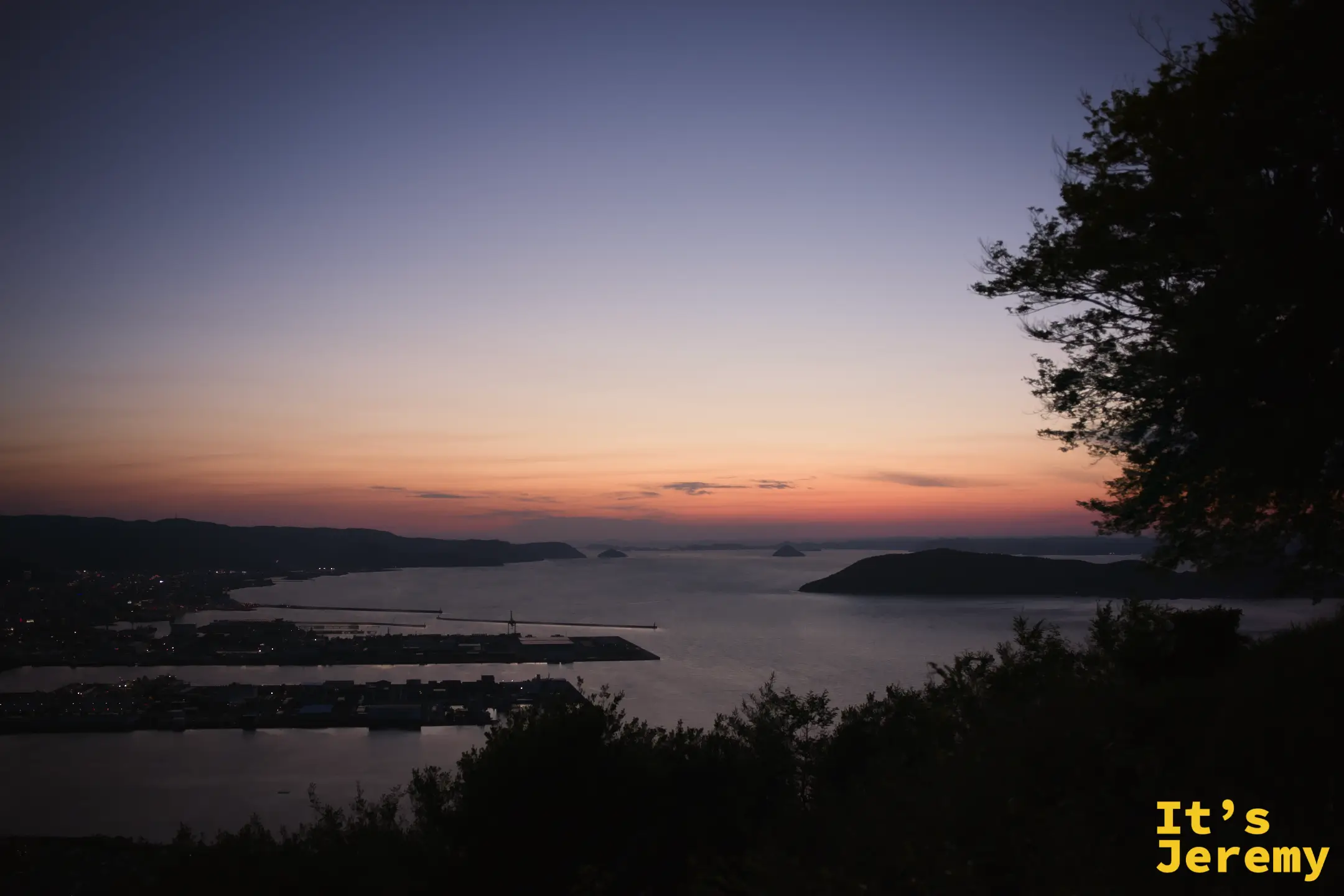 完全入夜，高松港燈光初現，天邊一線橙色餘暉，前景松樹剪影，海面漆黑而平靜
