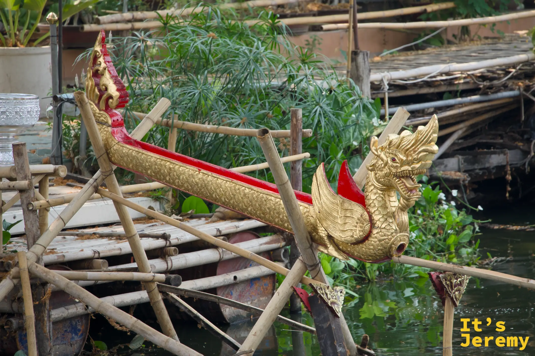 金色那伽龍舟裝飾架立於竹木支架上，頭部張口，旁邊是水道與植栽
