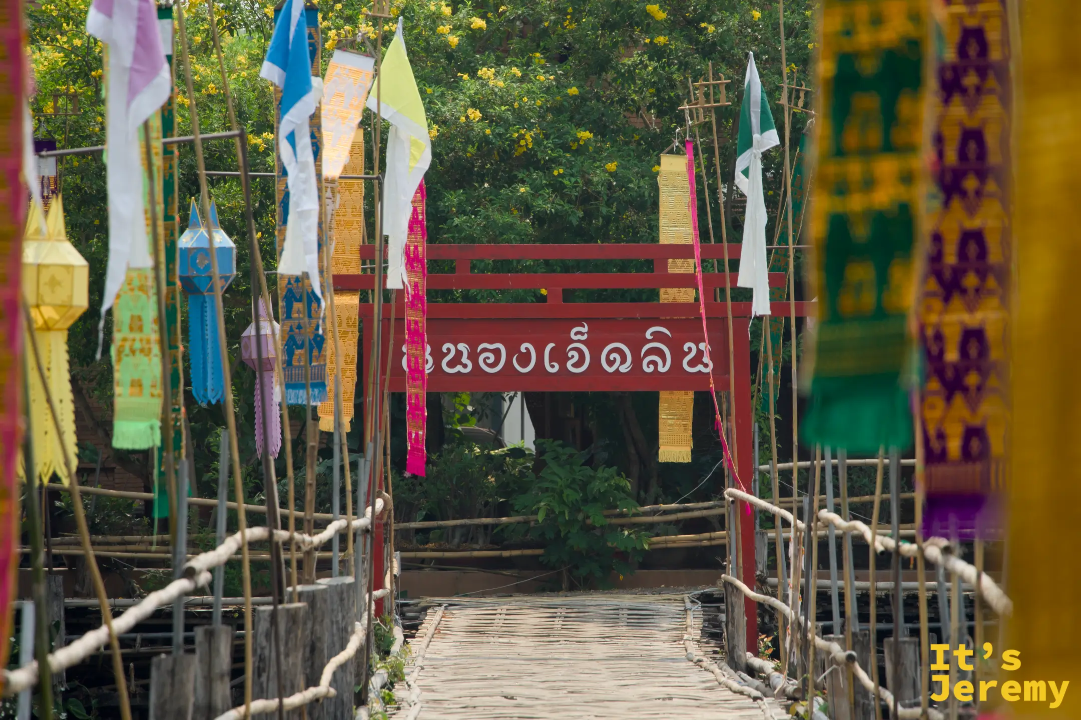 竹橋橫跨七林池，橋頭掛有紅色「หนองเจ็ดลิน」招牌，兩側布滿彩旗與燈籠