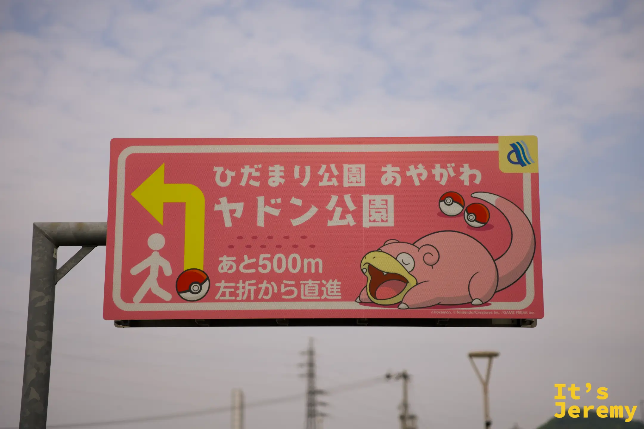 路旁粉紅底色的呆呆獸主題指路牌，寫著「ヤドン公園 あと500m 左折から直進」並印有寶可夢球圖案