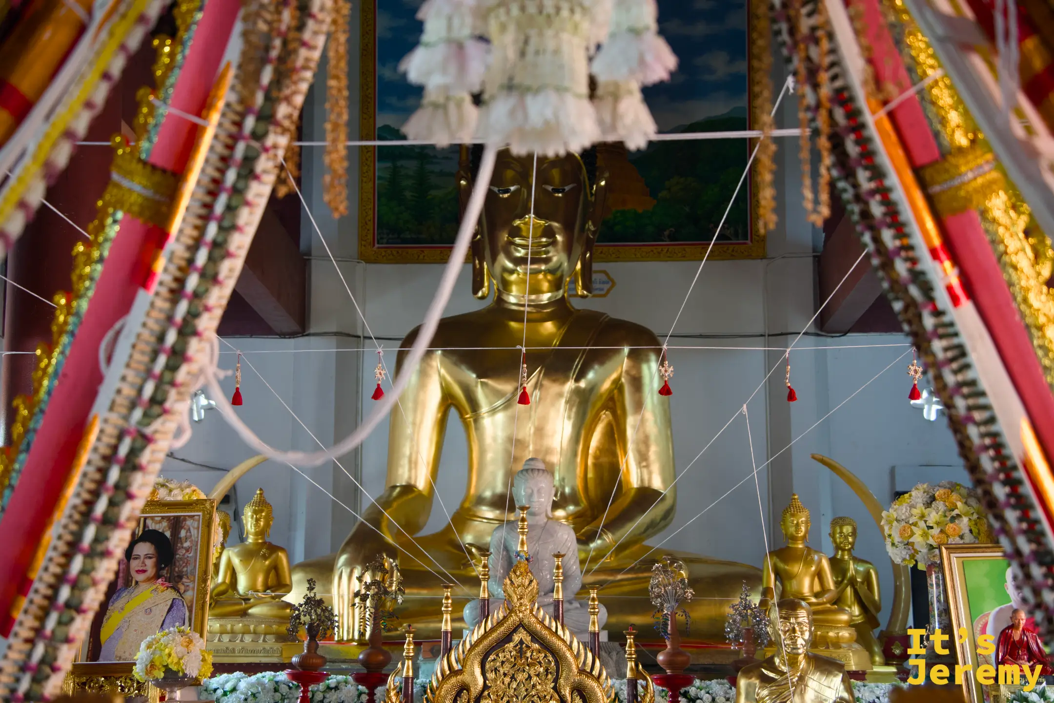 主殿大佛近景，頭頂垂掛白色花狀飾物，主佛兩側各有小型金佛護立，佛台欄杆紋飾繁複細膩