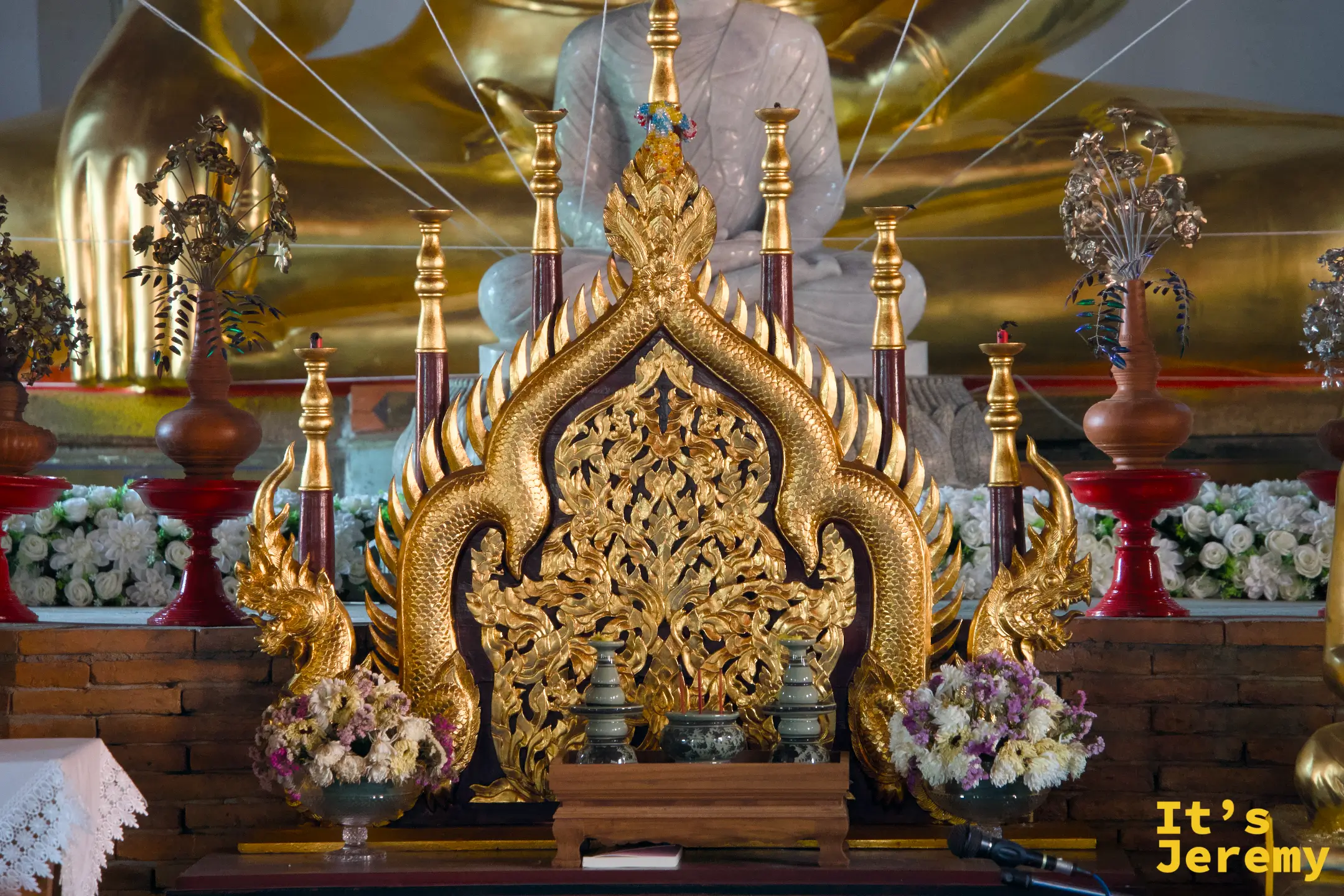 主殿祭台近景，金色那伽雙蛇守護台座兩側，台上供奉小型金佛，周邊花環鮮花點綴，台後可見大型佛像輪廓
