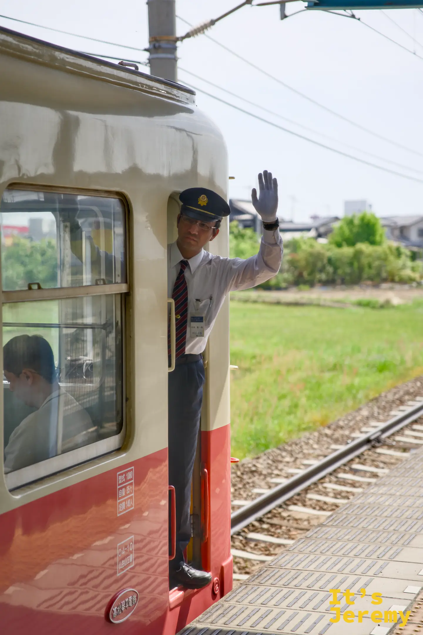奶油色列車車廂的車長從車門探出頭，戴著白手套舉手確認發車安全