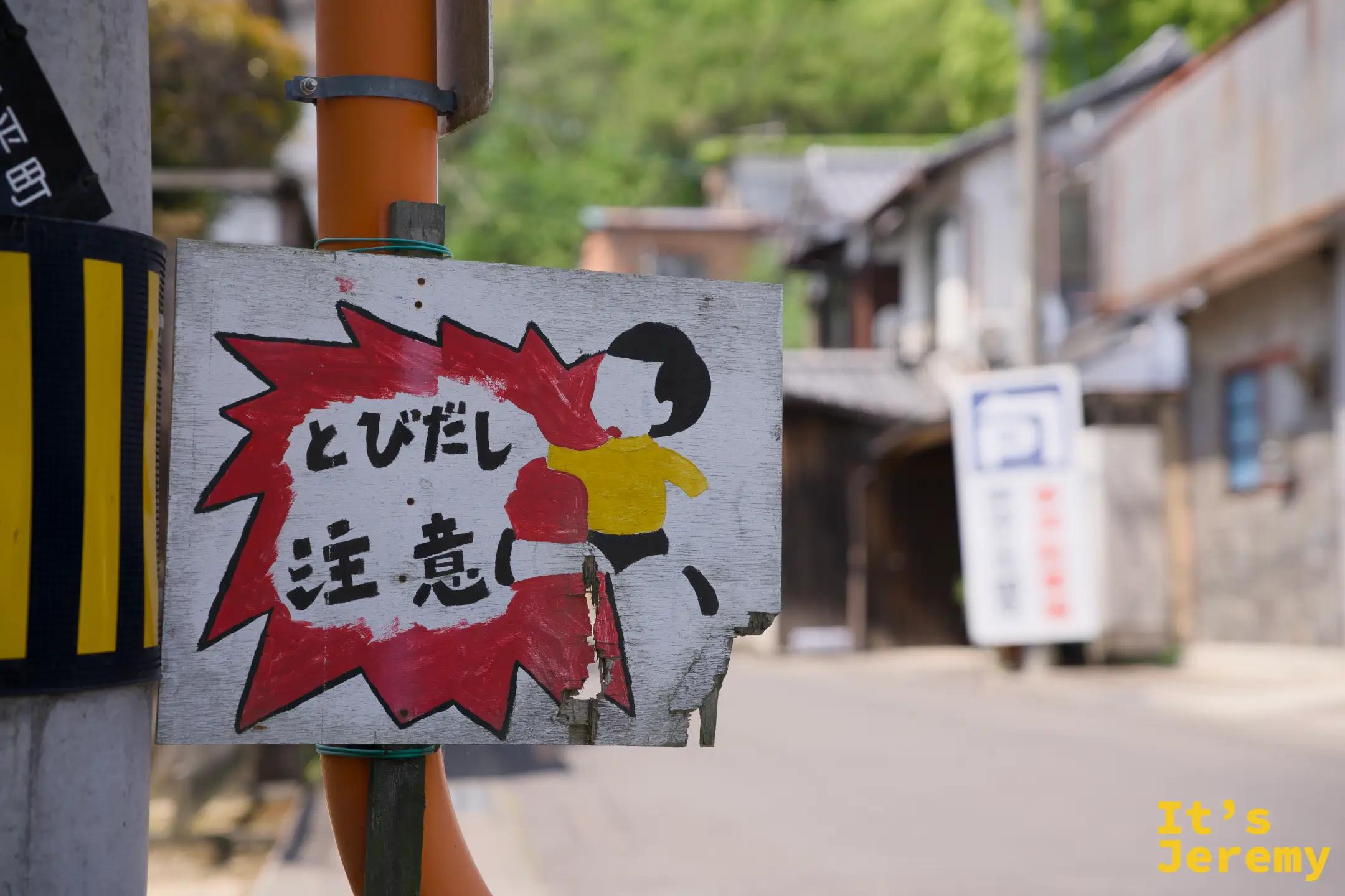 電線桿上掛著「とびだし 注意い」紅色爆炸圖案木牌，飛び出し坊や衝刺圖像清晰可辨