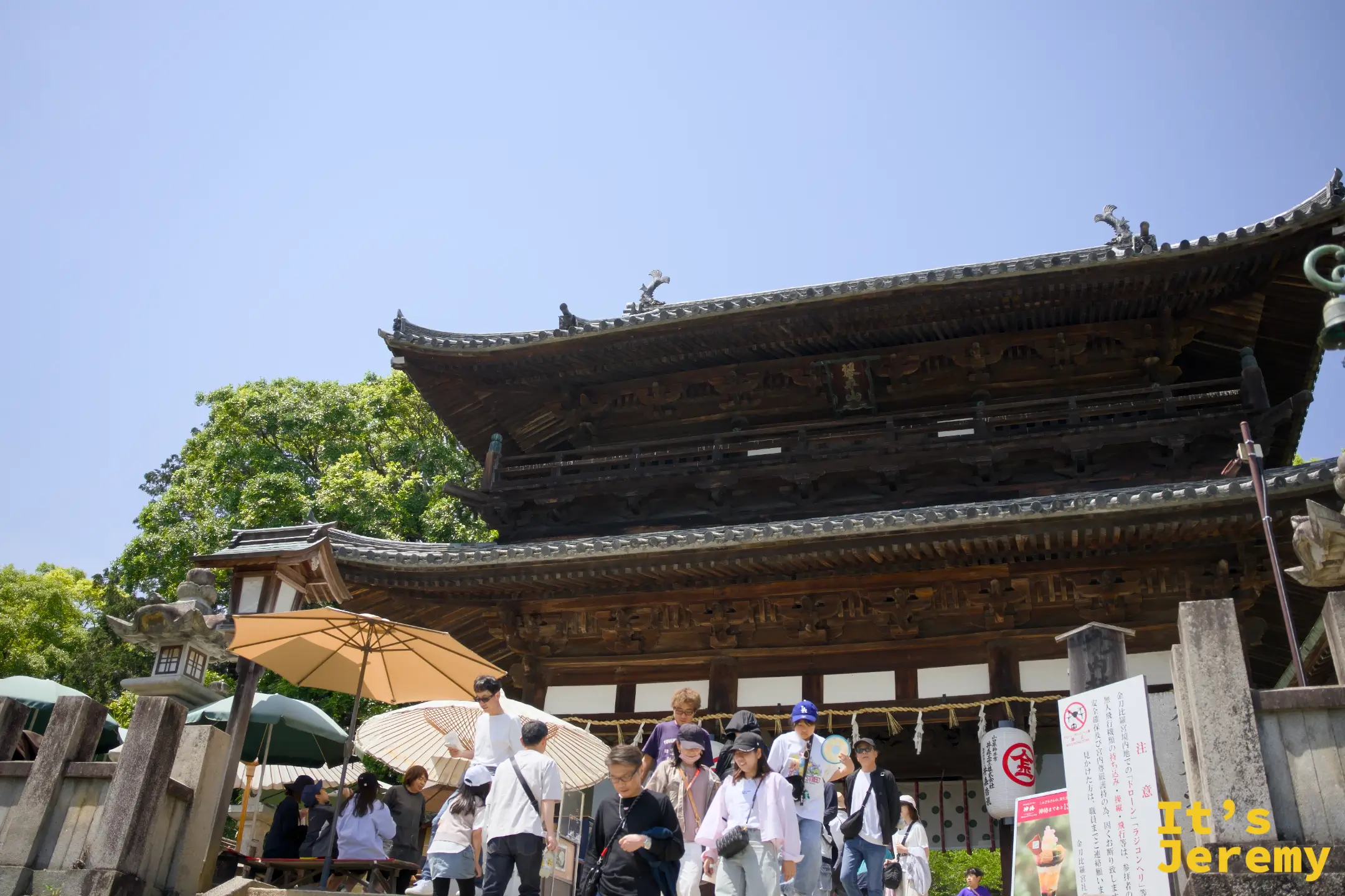 表參道的入口大門，雙層飛檐的木造建築前聚集了許多參拜者，燈籠和傘點綴其中