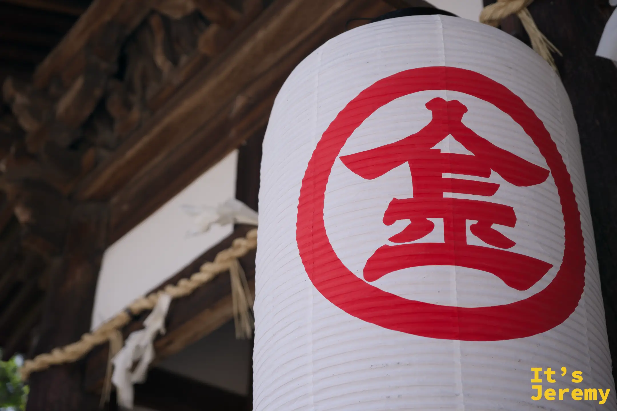 近拍境內的白色燈籠，上面印著朱紅色的「金」字金丸印，背景是神社木構架和注連繩
