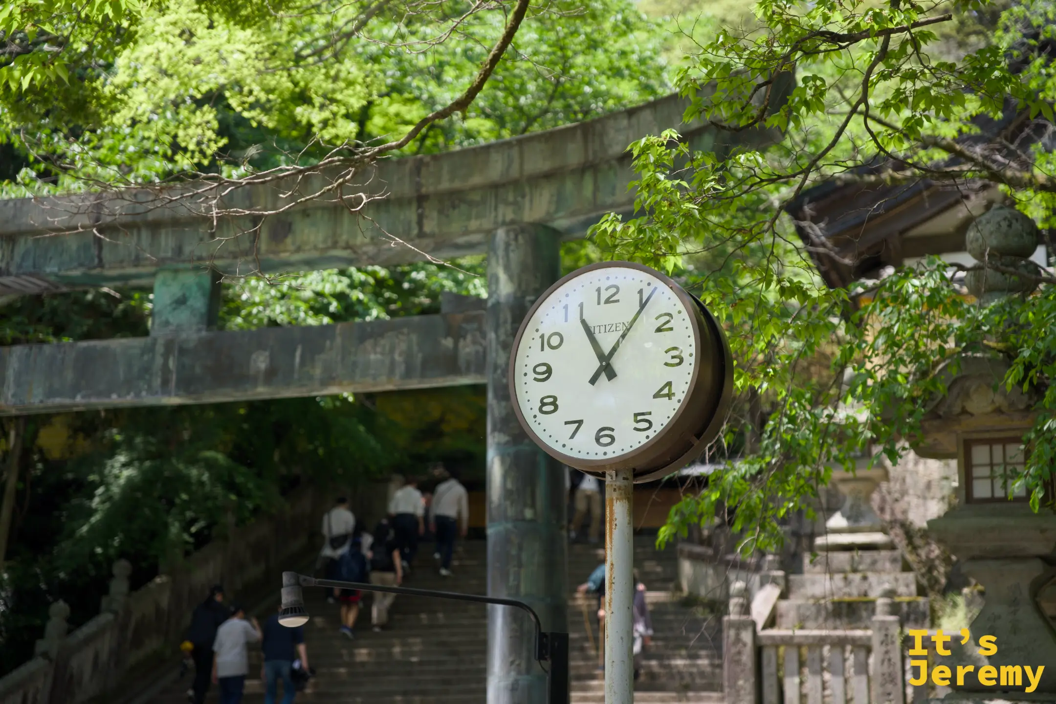 表參道上的 CITIZEN 圓形時鐘，背景是青銅色的鳥居和往上延伸的石階