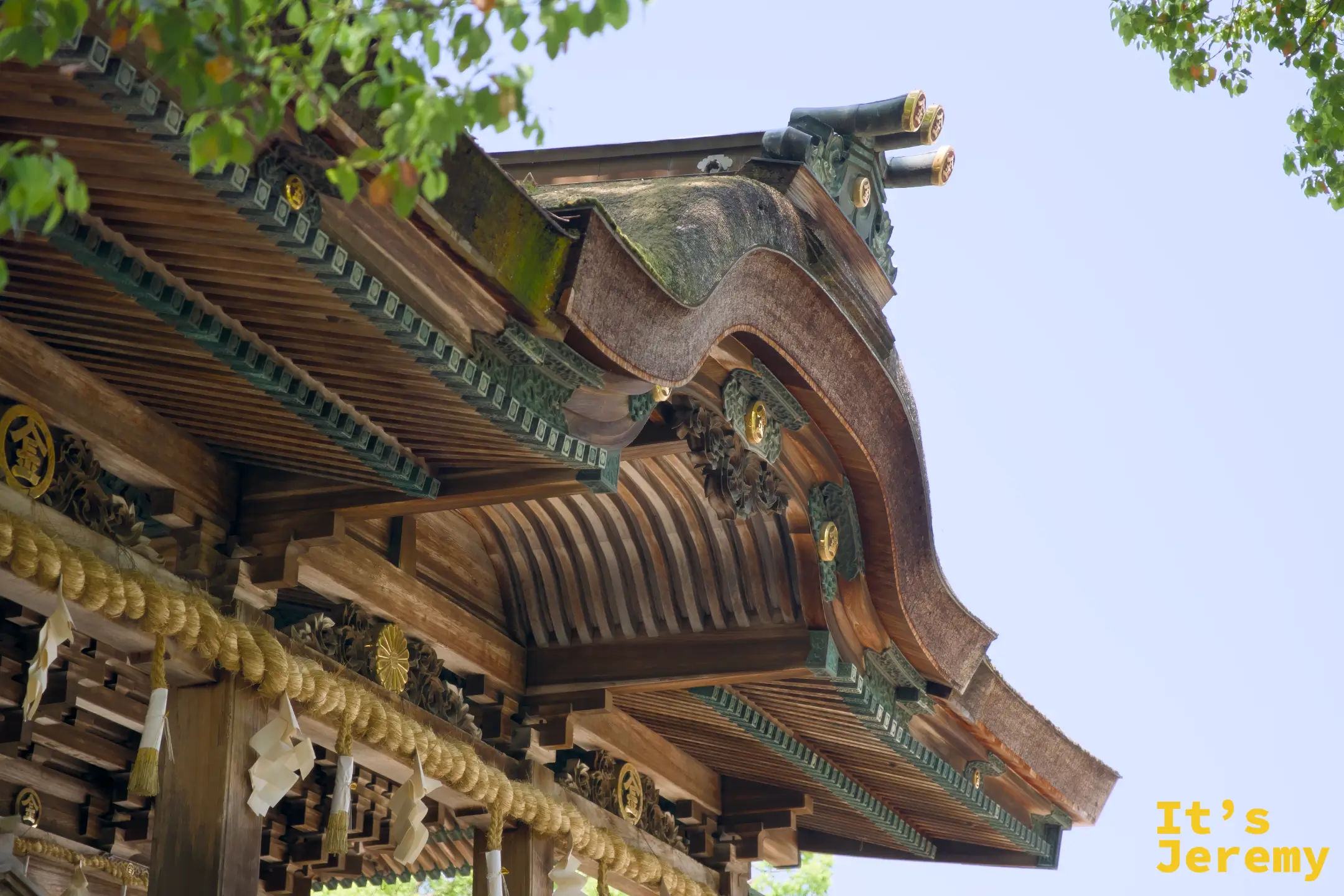 御本宮的唐破風屋頂仰拍，金色裝飾與青銅綠色瓦片，注連繩和紙垂在廊下垂掛