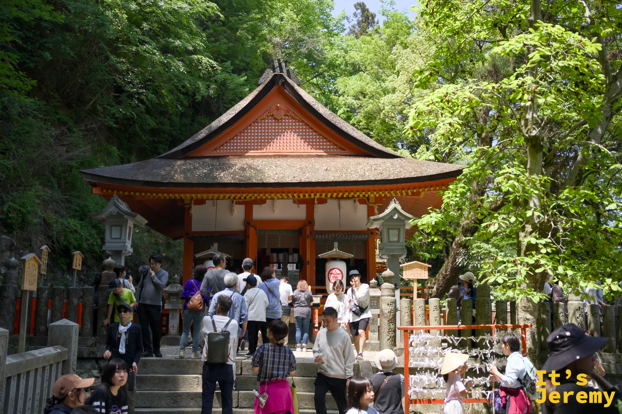 厳魂神社（奧社）全景，朱紅色建築在密林環抱中，石燈籠排列，人群在前方聚集