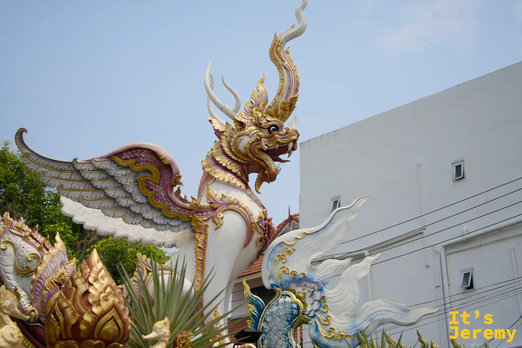 大門一側屋簷的神獸特寫——白色鱗身、金色翅膀、牛角，盤踞在屋角，後方是古城建築的白牆