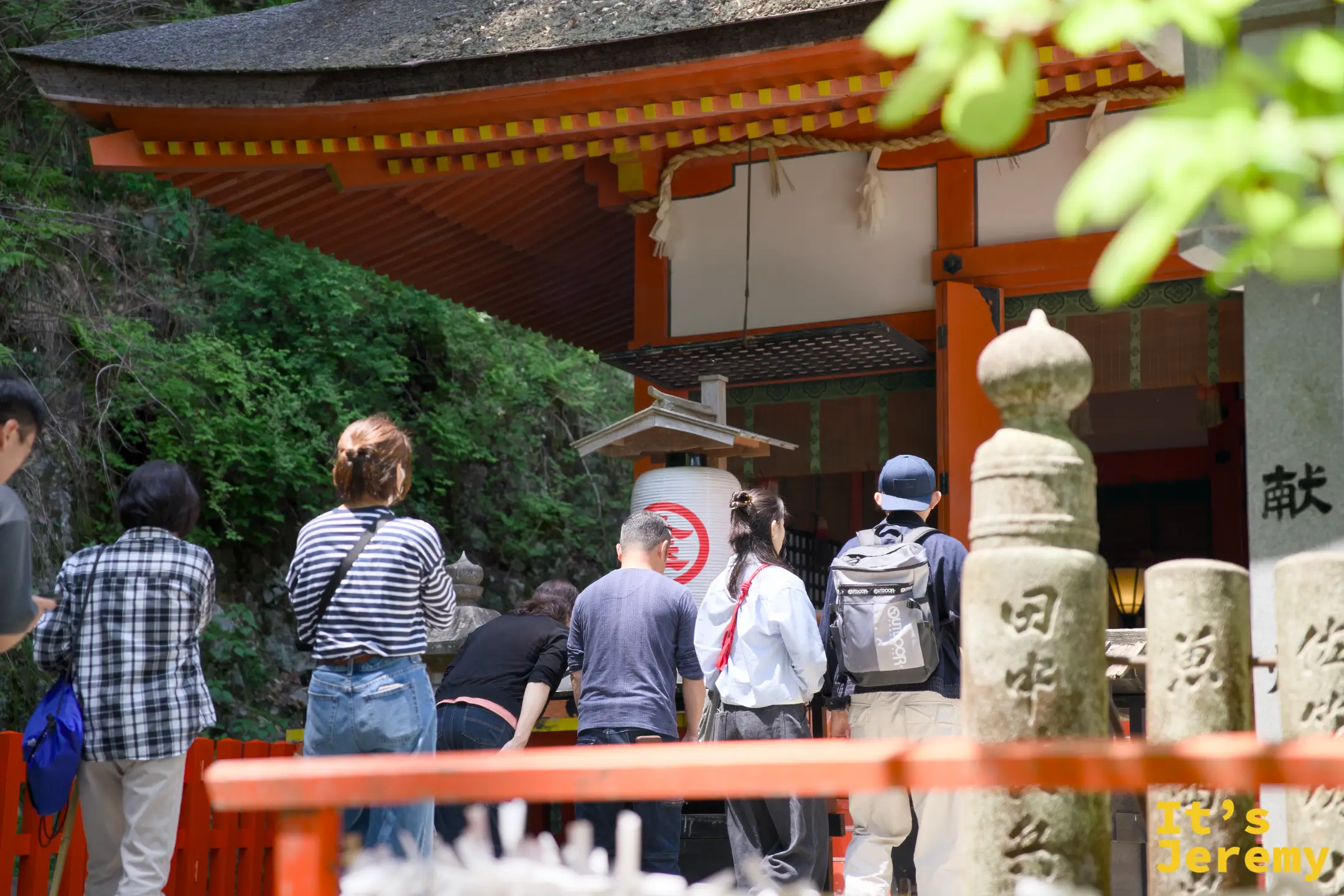 從紅色欄杆和石燈籠間望向厳魂神社正殿，参拜者排成小隊等候