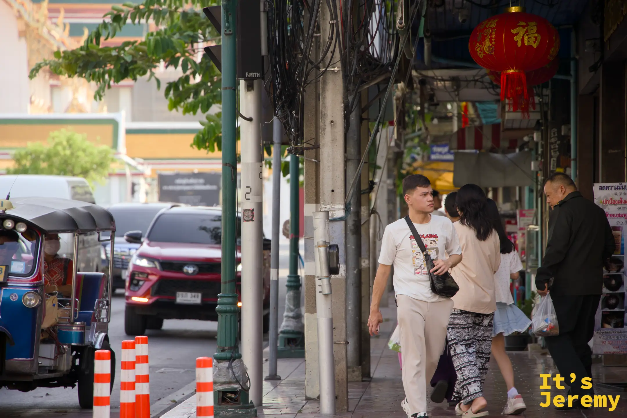一對年輕情侶走過街角的「福」字紅燈籠下、藍色嘟嘟車停在背景，傍晚老城區的標準畫面