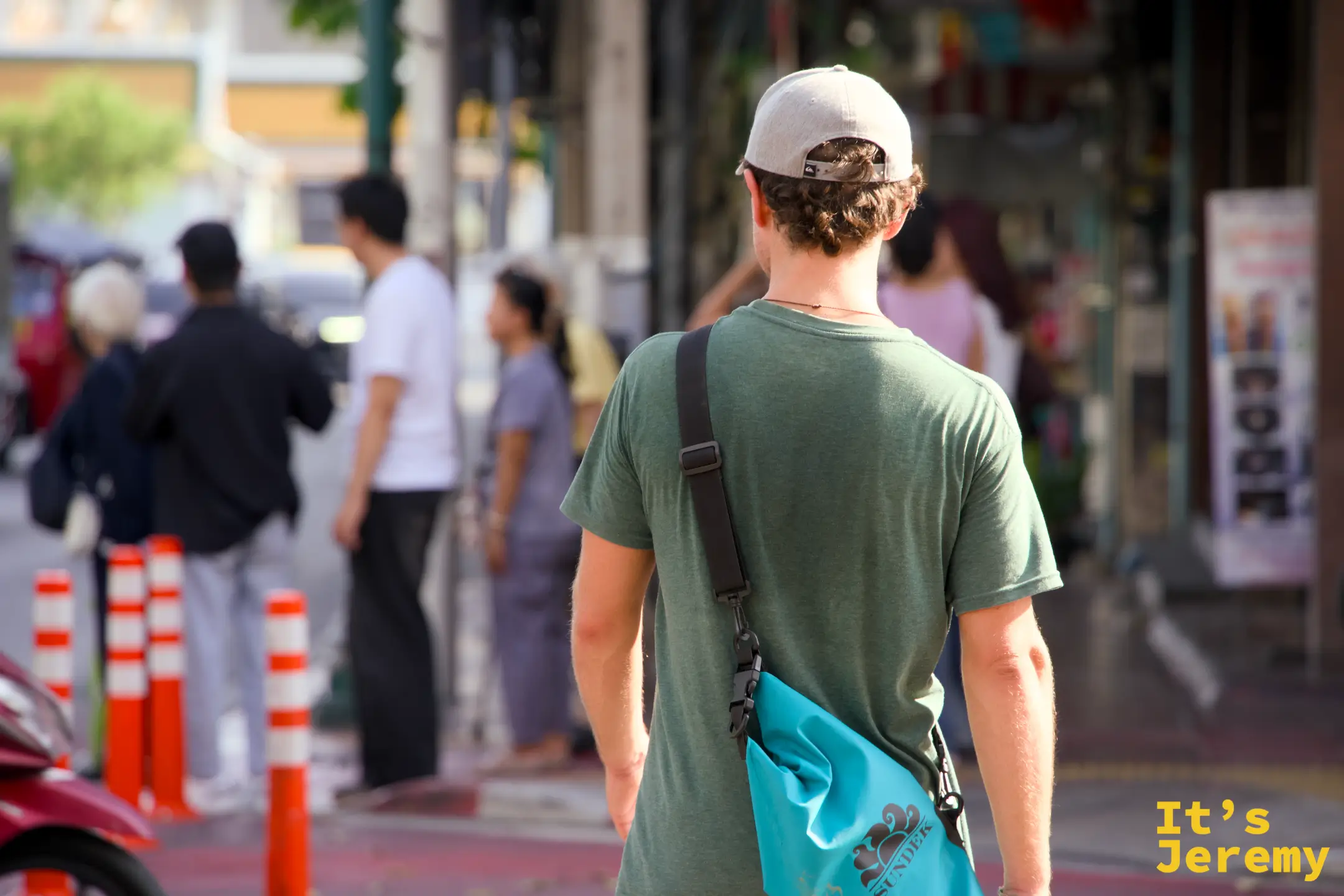 一位戴著淺色 Quiksilver 帽的外國背包客背對鏡頭、肩上掛著薄荷綠 Sundek 隨身包——這條動線會吸引這種「攝影派背包客」的旅人