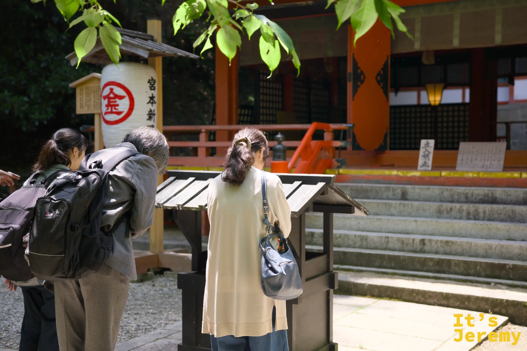 三名參拜者背對鏡頭，靜靜在白峰神社前合十，紅色建築在背景中清晰可見