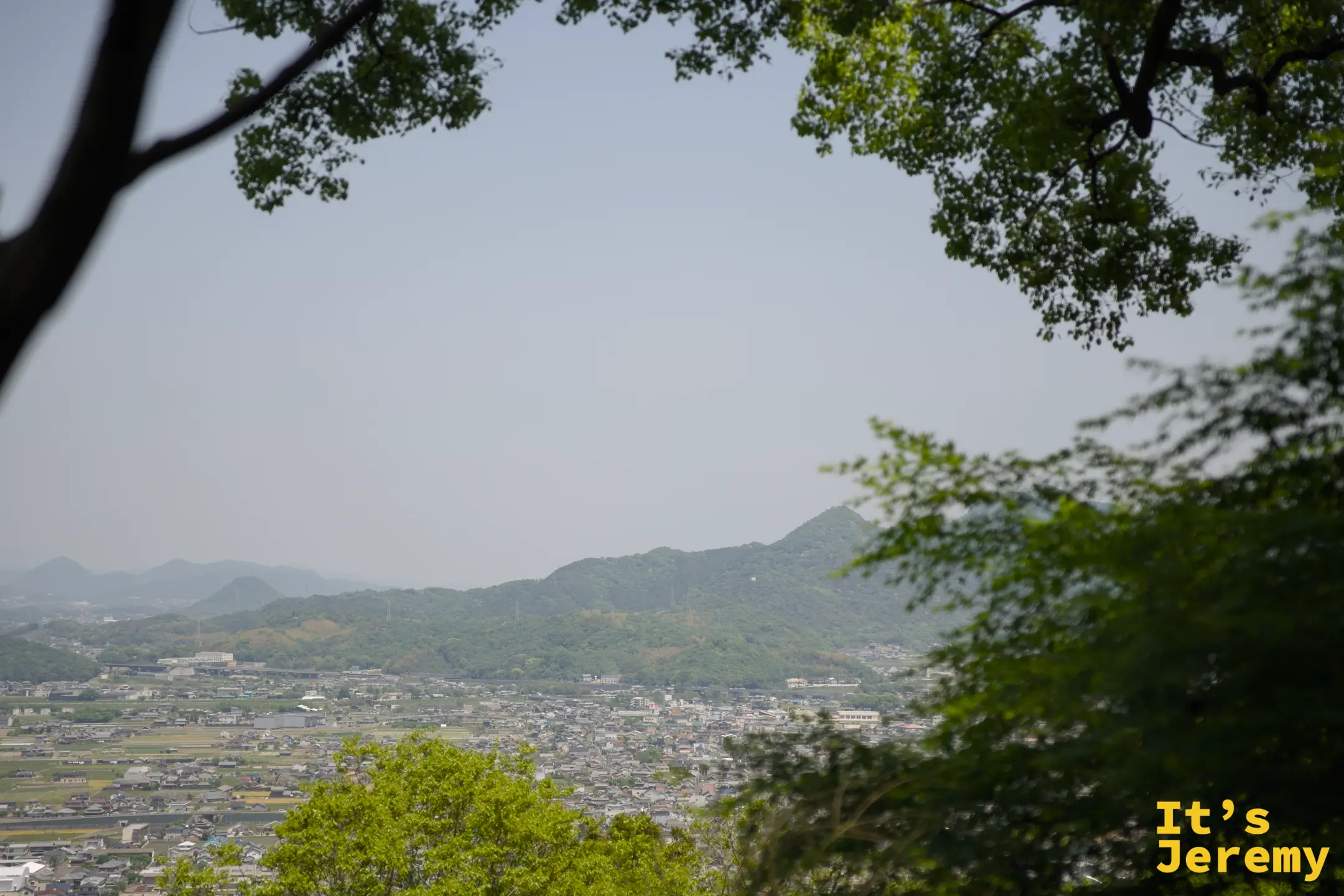 穿過樹枝間隙望見讚岐平野的遠景，藍天和山脈清晰可見