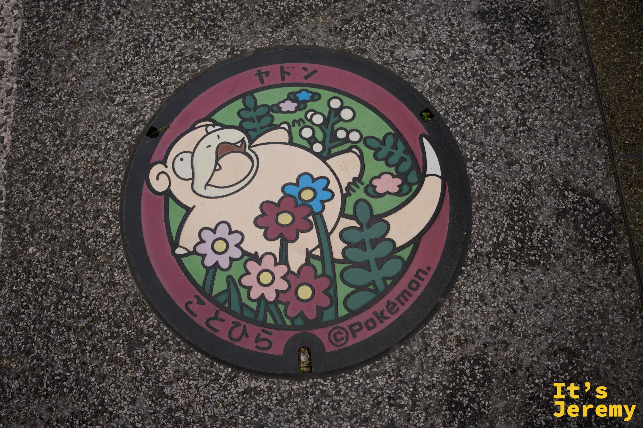 圓形人孔蓋，呆呆獸仰躺於花草間，外圈印「ヤドン」與「こんぴら」字樣