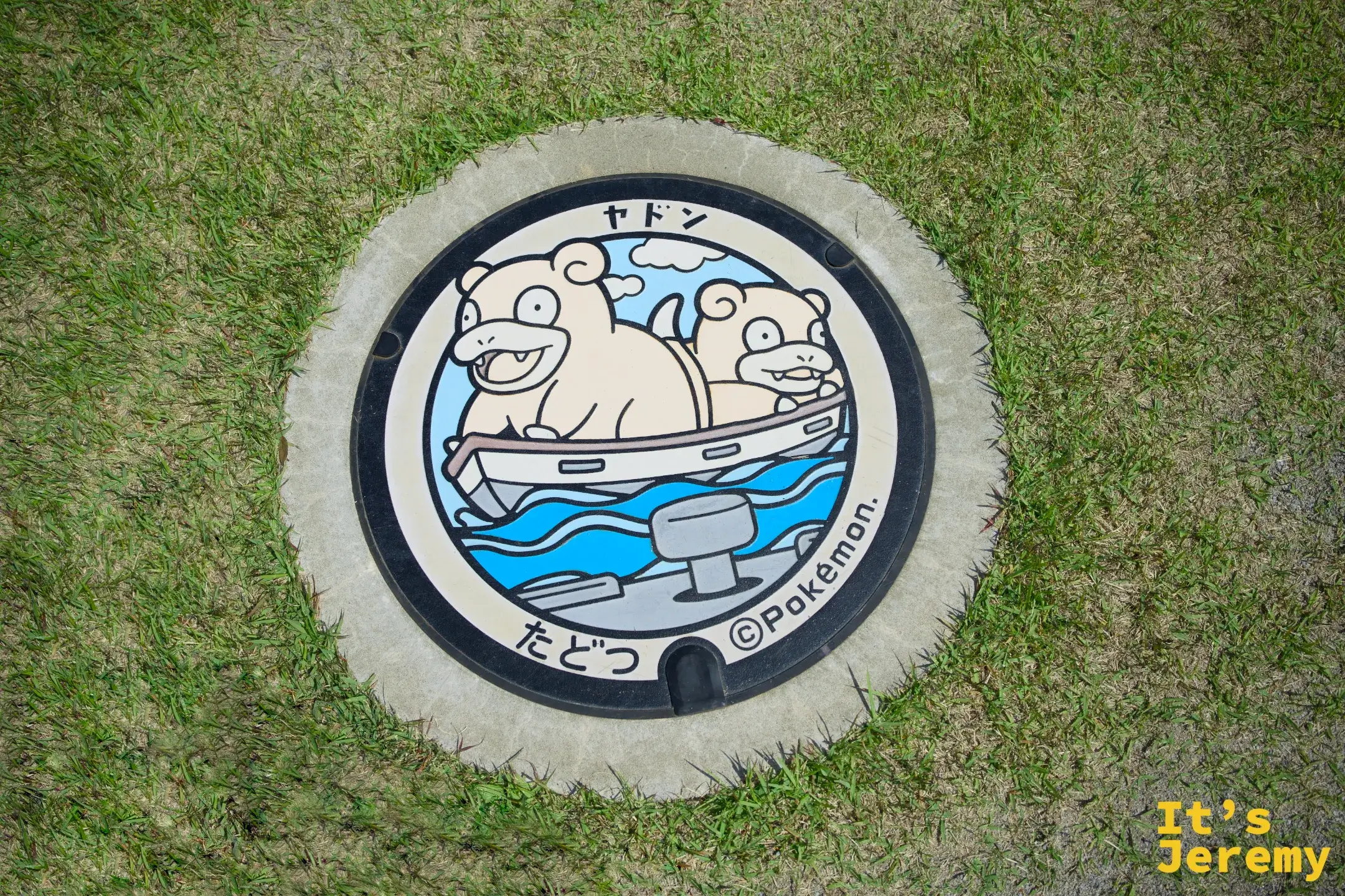 圓形人孔蓋鑲嵌於草坪旁，呆呆獸坐船於水面，外圈印「ヤドン」與「たどつ」字樣