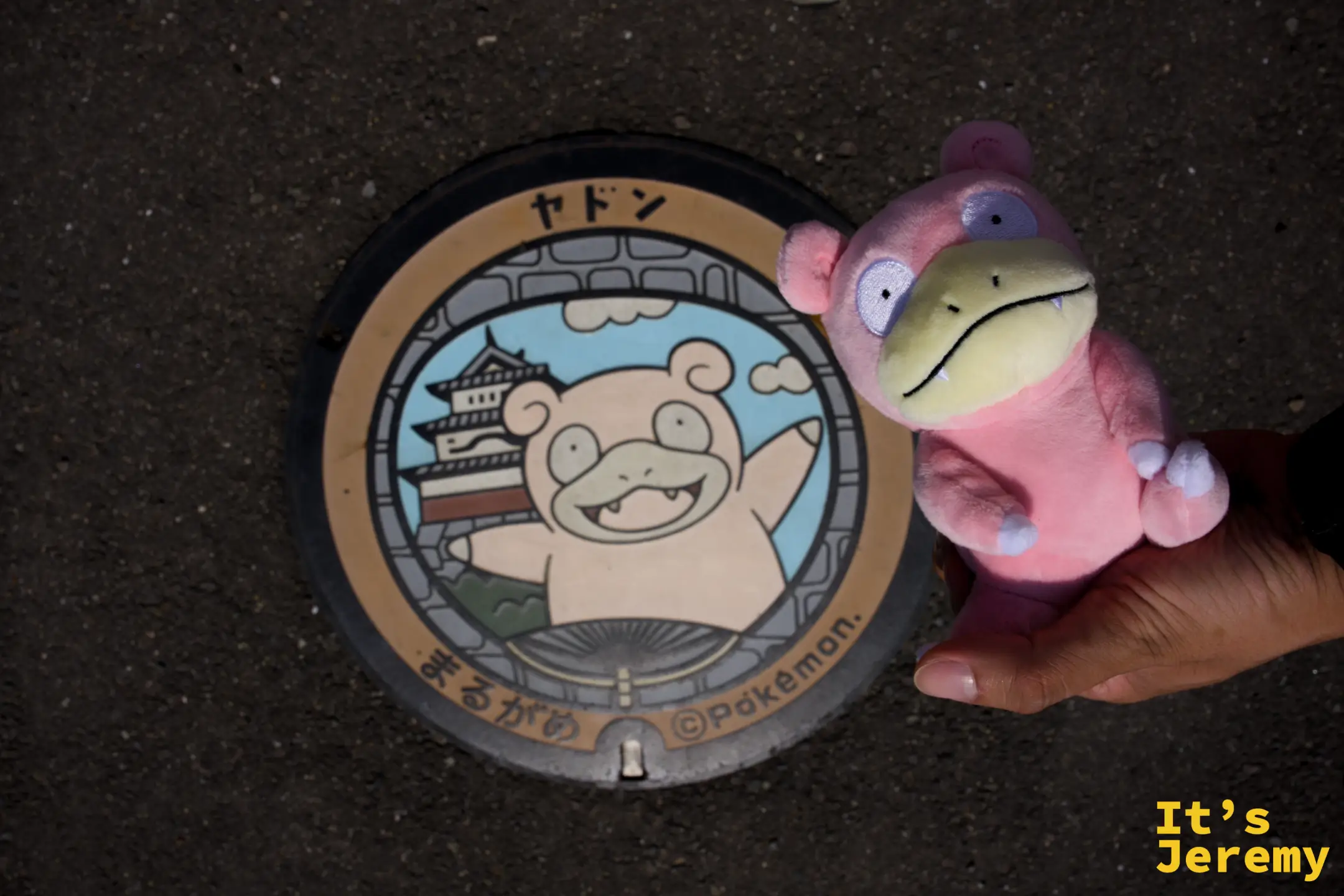 手持呆呆獸玩偶在丸亀市人孔蓋旁合照，玩偶面向蓋面上的呆呆獸