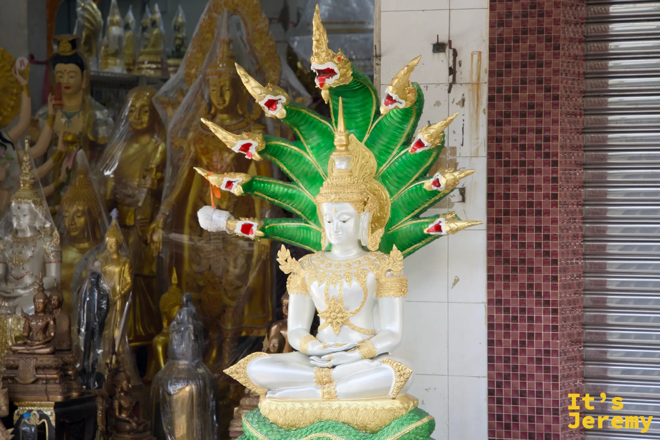 店門口立著一尊白色佛像、頭頂上是七條綠色那伽蛇神光環，這是泰國最具代表性的造像之一