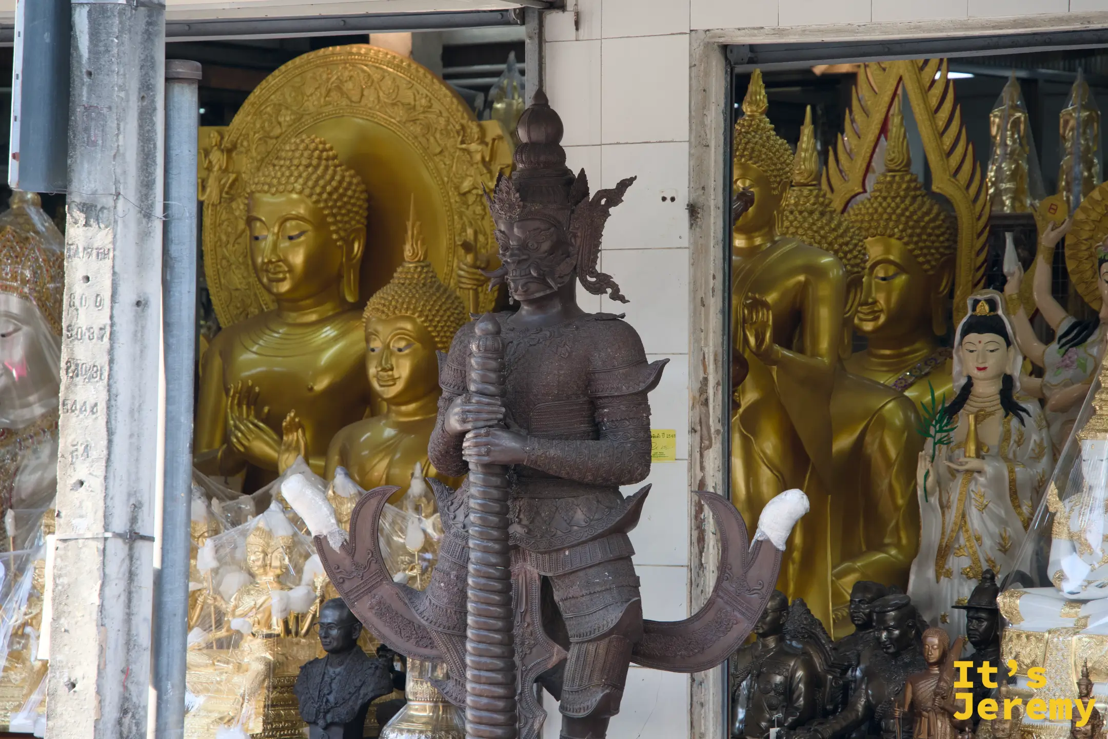 另一家佛具店的青銅戰神塑像，背景是一整面金色佛像