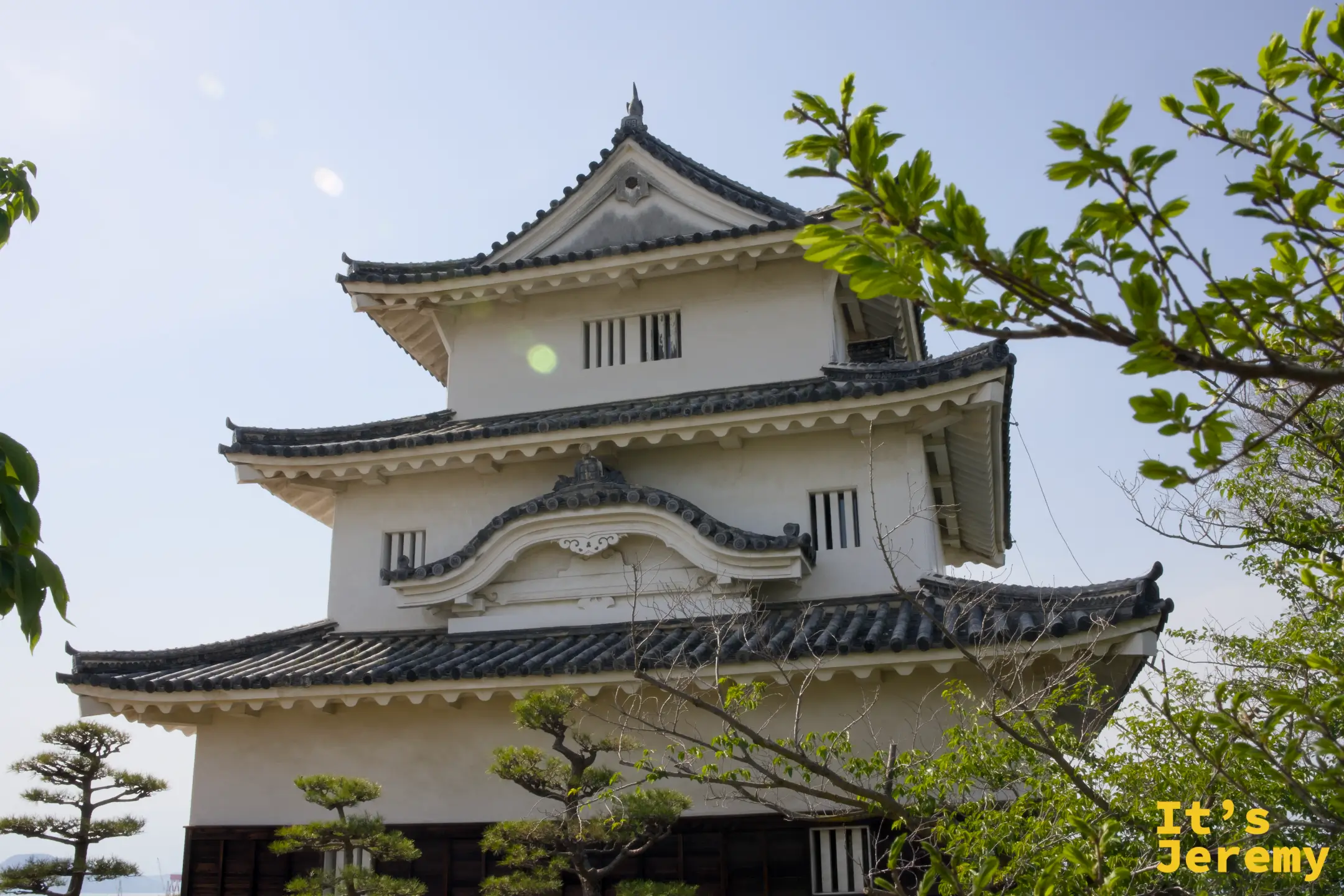 丸亀城天守閣全景，三層白牆木構建築，松樹環繞