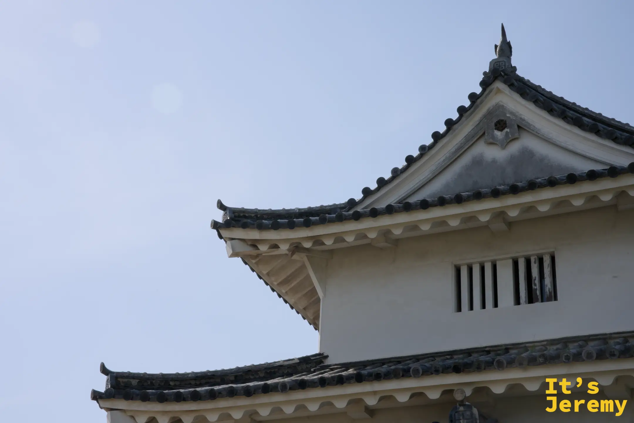 丸亀城天守低角度仰拍，白色牆壁與灰黑瓦片在藍天下對比強烈，飛檐層疊