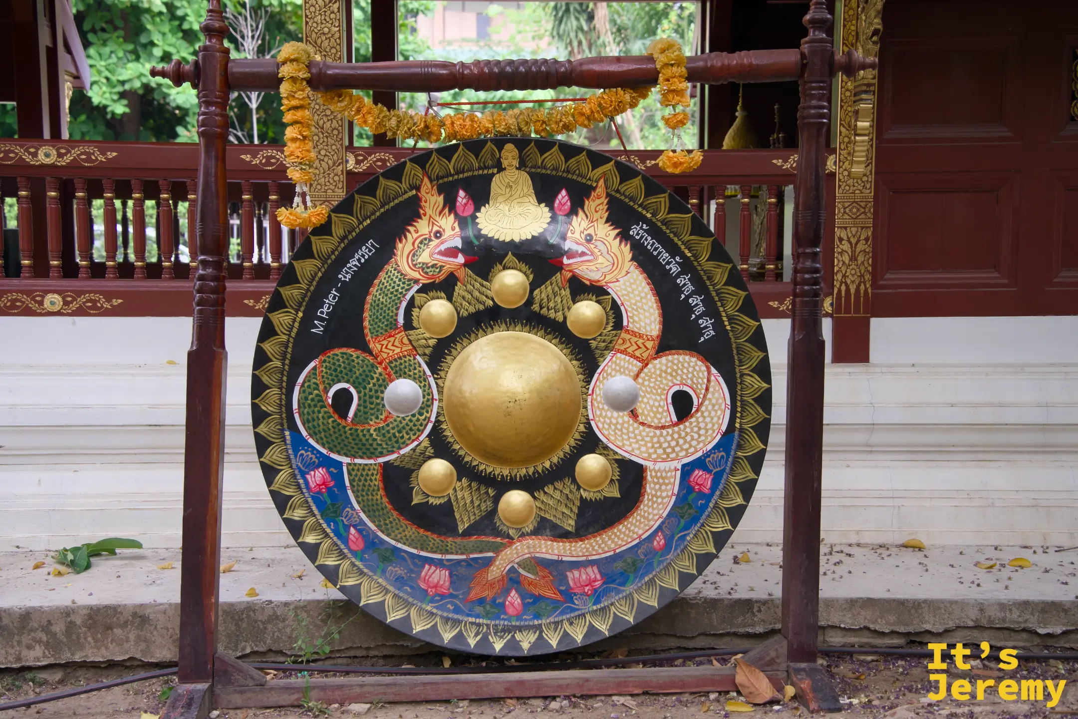 大銅鑼，黑底金色雙龍與蓮花圖案，上掛橘色萬壽菊花環