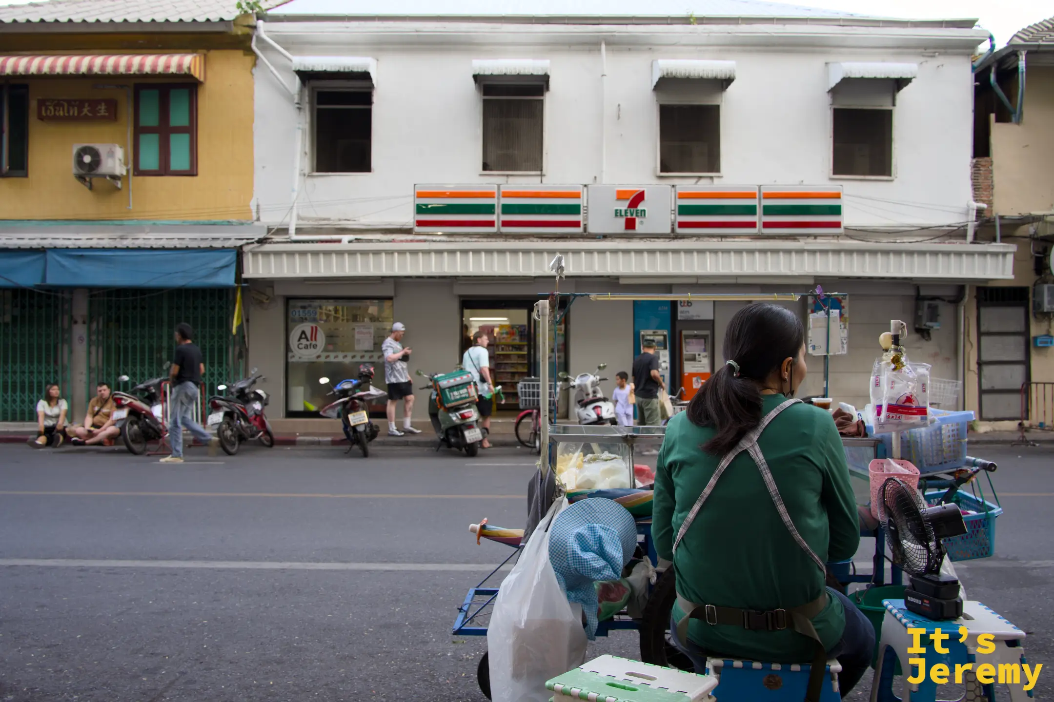 7-Eleven 對街賣涼粉的阿姨推車與背對鏡頭的剪影，便利商店與街邊小販的並存