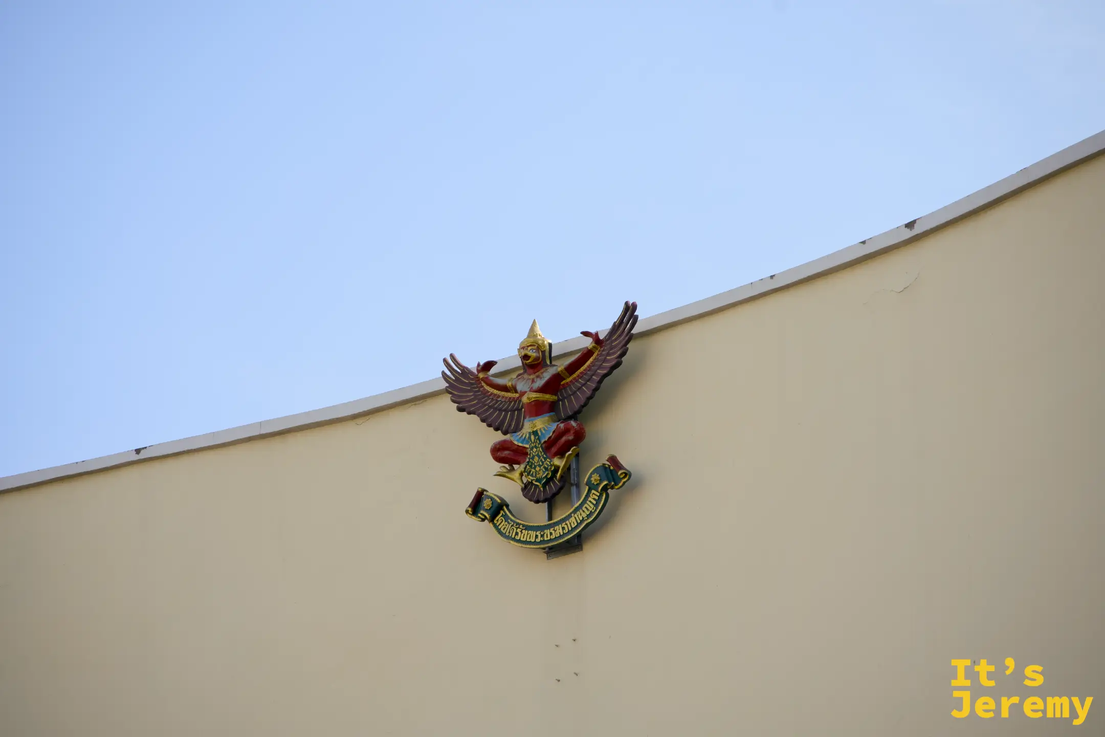 一棟米黃色官方建築外牆掛著的金翅鳥（Garuda）雕飾，這是泰國皇家機構的象徵