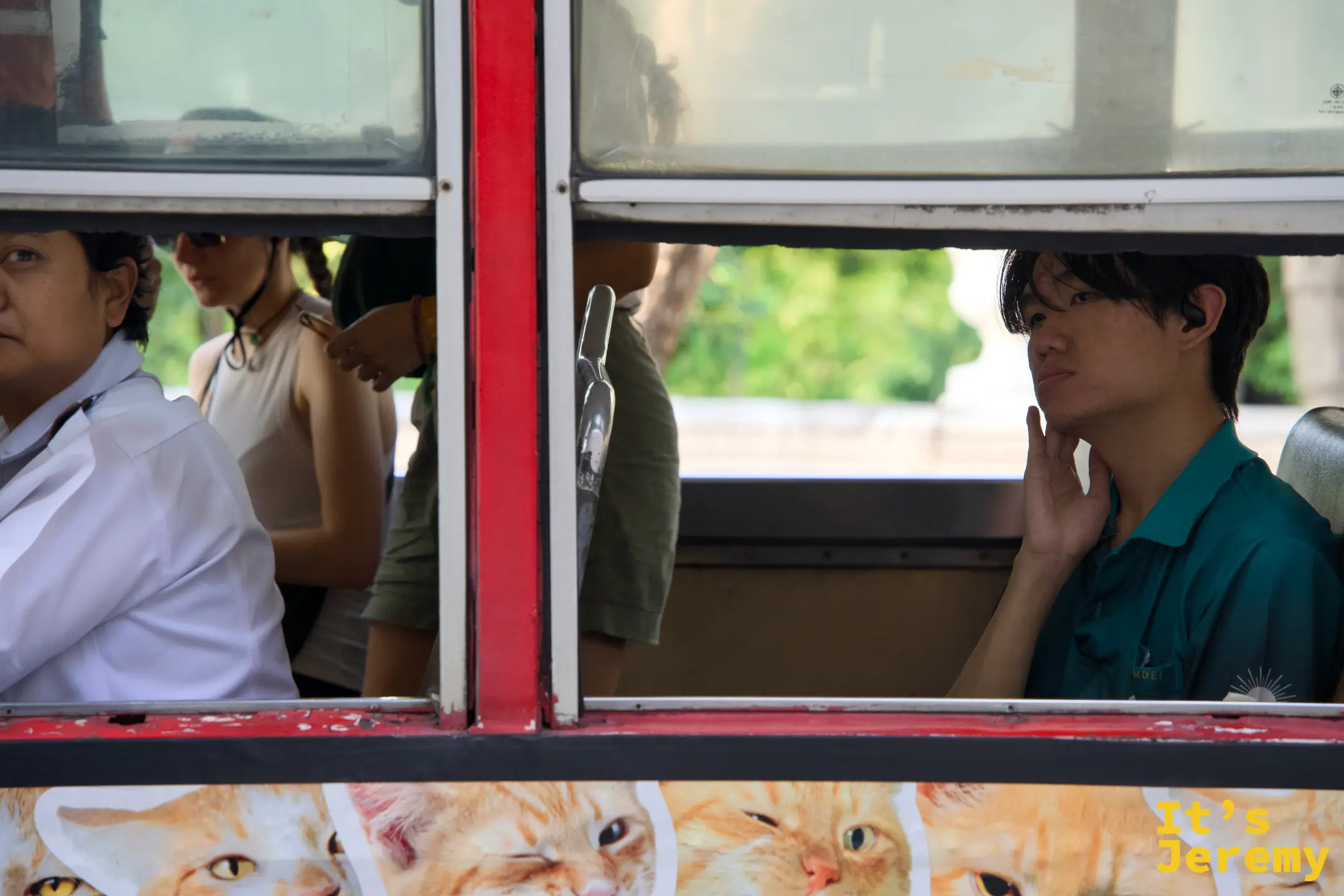 一輛 tuk-tuk 後座窗框上、一個男生用手指撐著下巴、車身畫滿橘色貓咪——曼谷 tuk-tuk 文化的剖面
