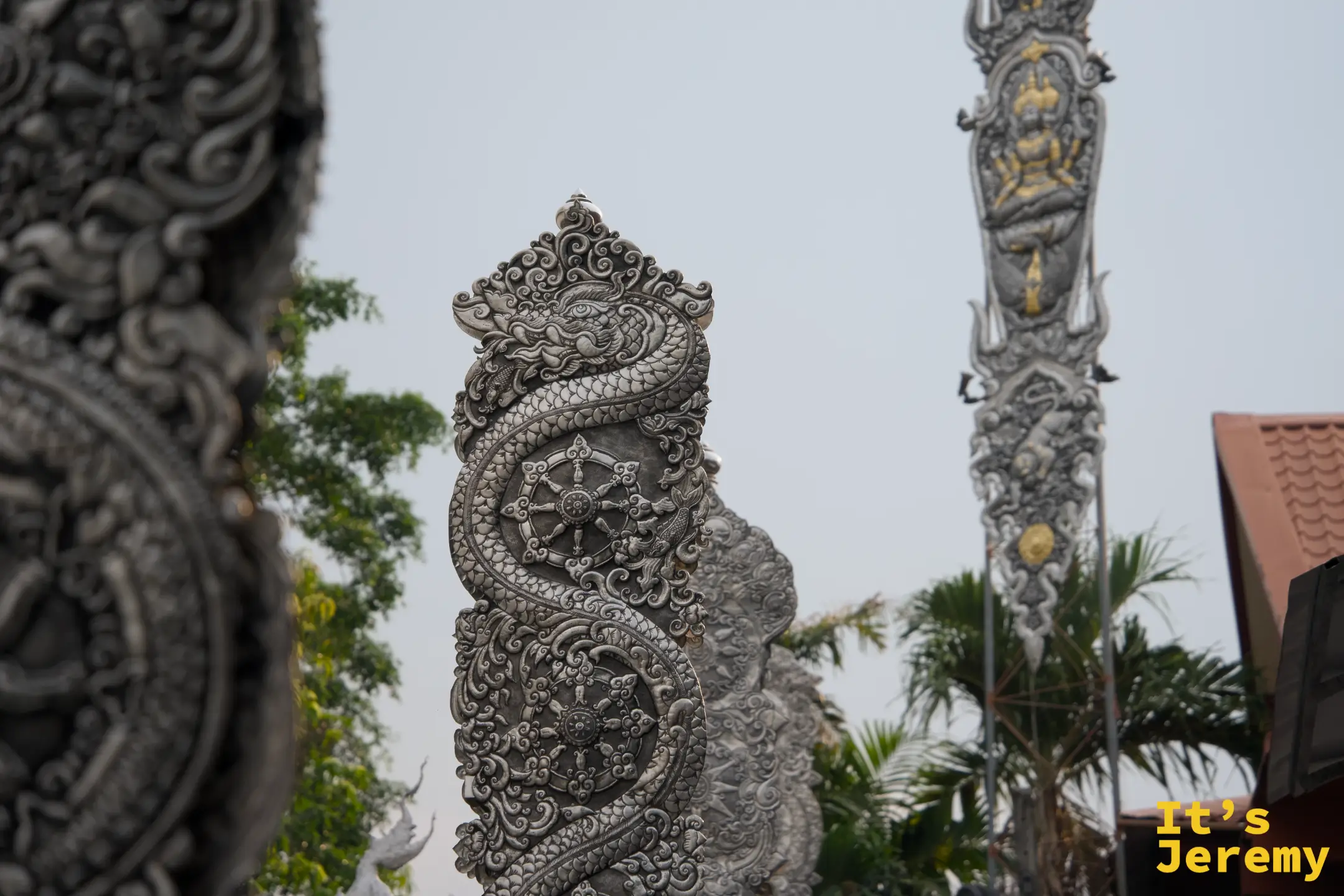 銀色裝飾柱，螺旋蛇身纏繞配上法輪圖案，右後方可見另一根旗幡柱