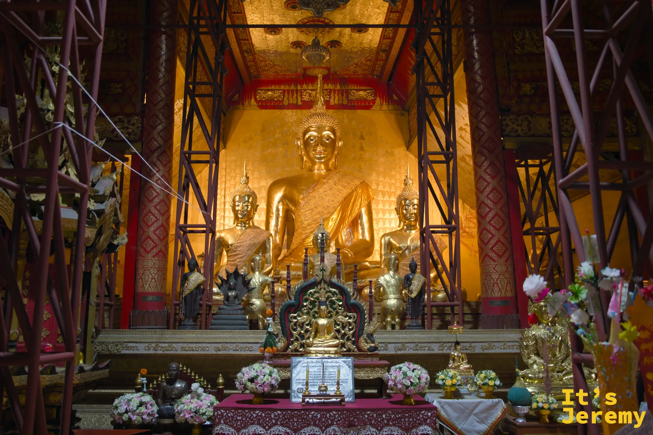 佛堂主佛壇，大型金色坐佛居中，兩側各有侍立佛像，供品花環包圍