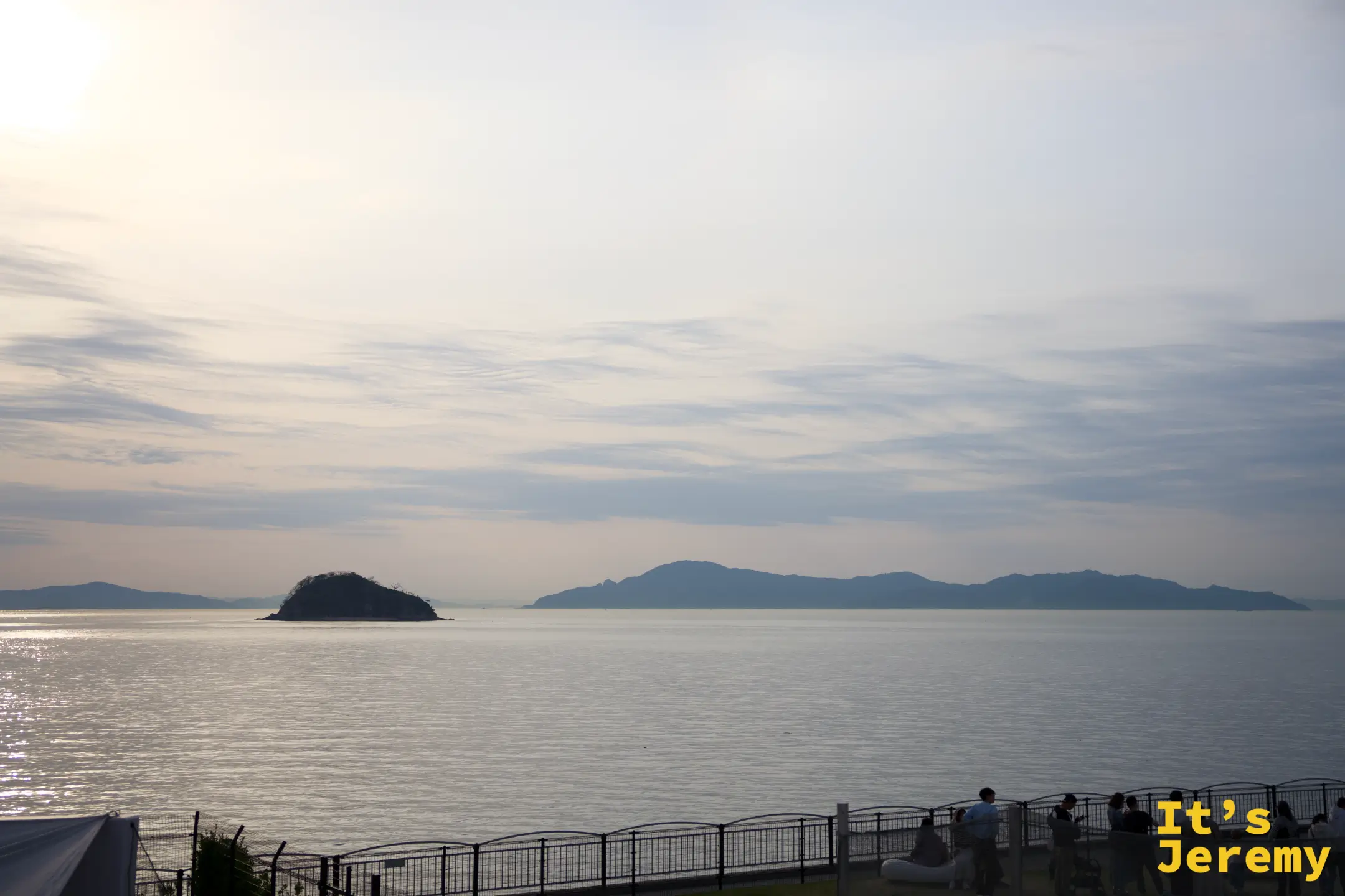 瀨戶內海日間景色，遠處有兩座島嶼輪廓，前景有欄杆和幾個人影
