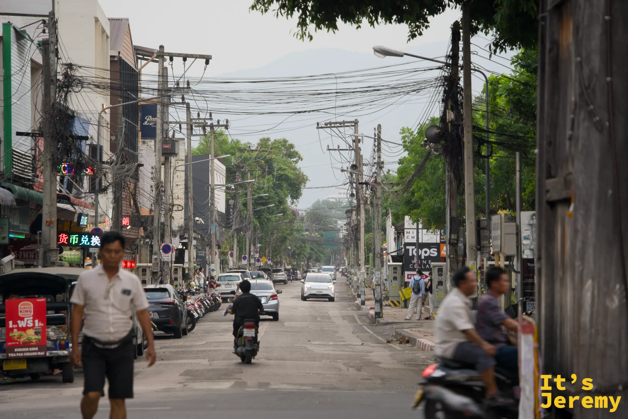 清邡城區主幹道，行人與摩托車共用道路，電線交錯，遠山在城市輪廓後方隱現，是清邡很典型的一幅景